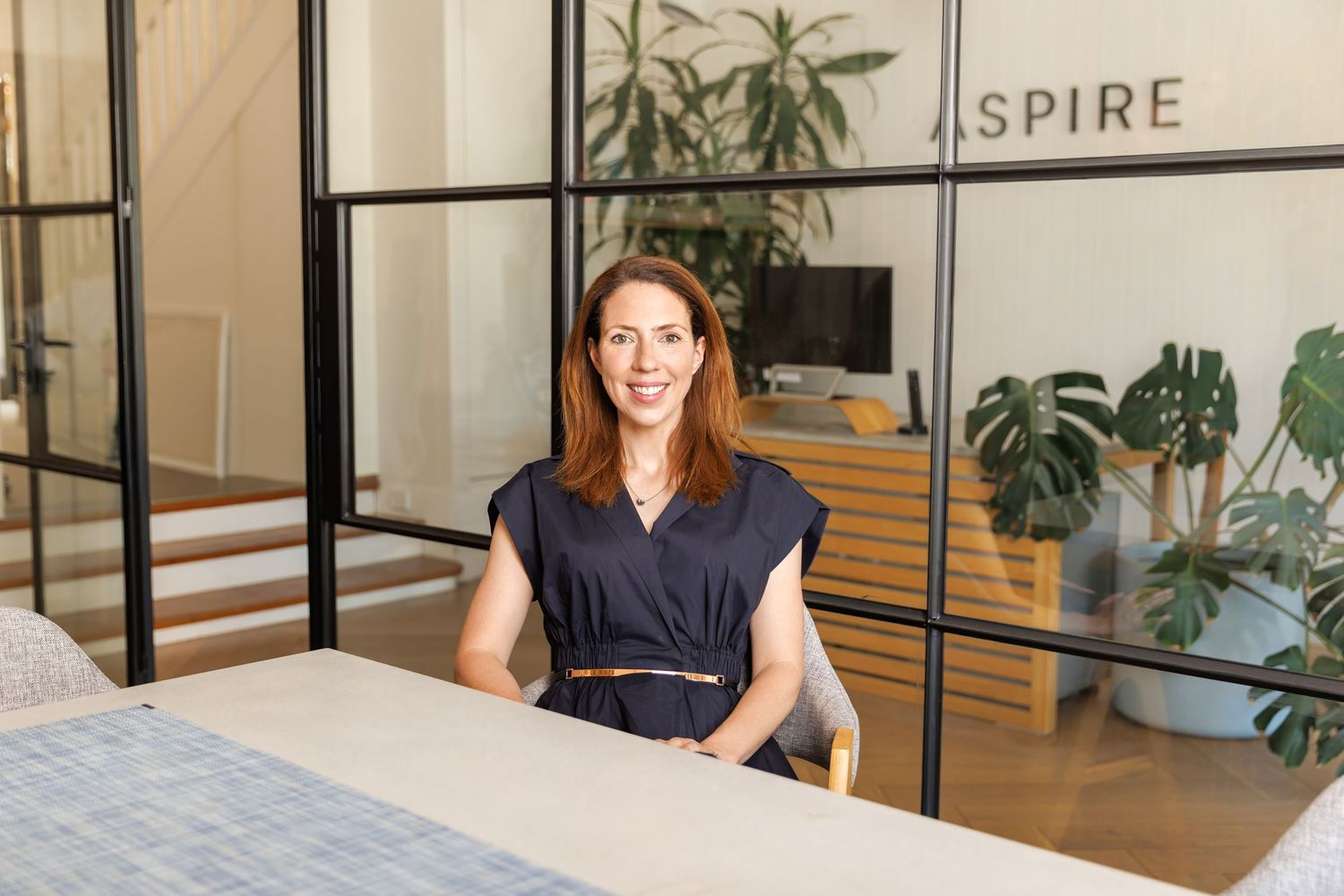 Professional business portrait of a woman in a modern office interior with plants, soft natural light and neutral tones.