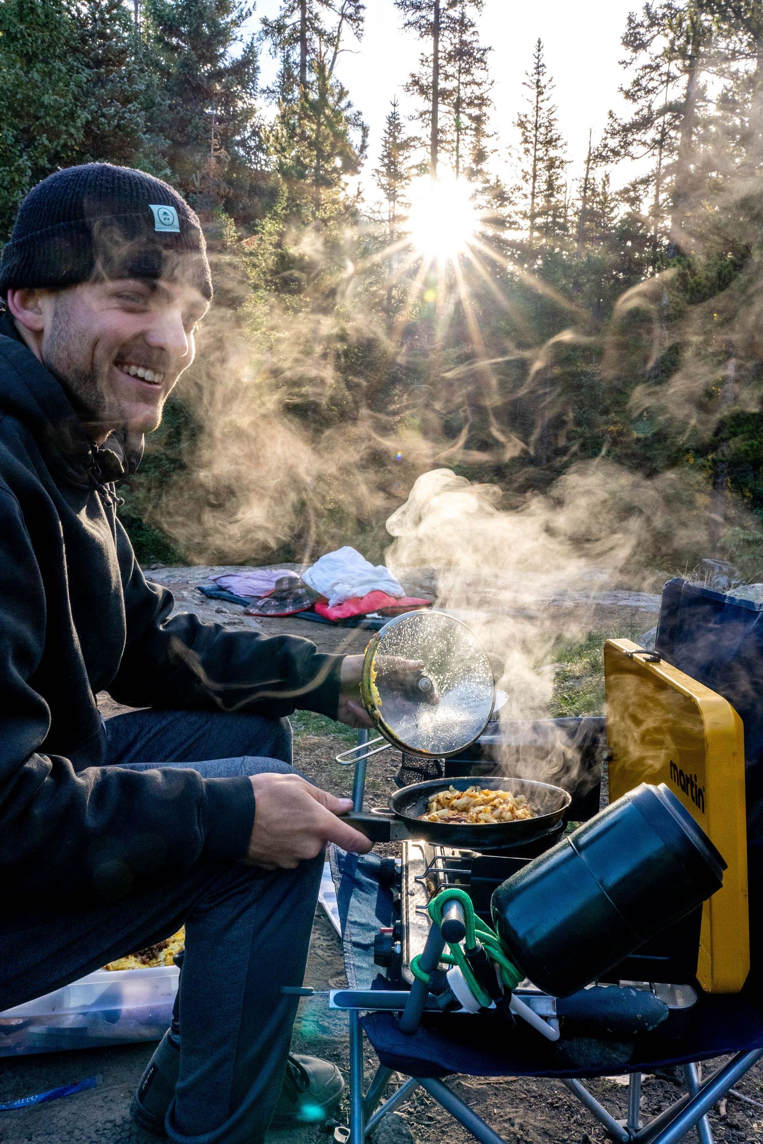 man cooking with smoke billowing from the stovetop at a campsite