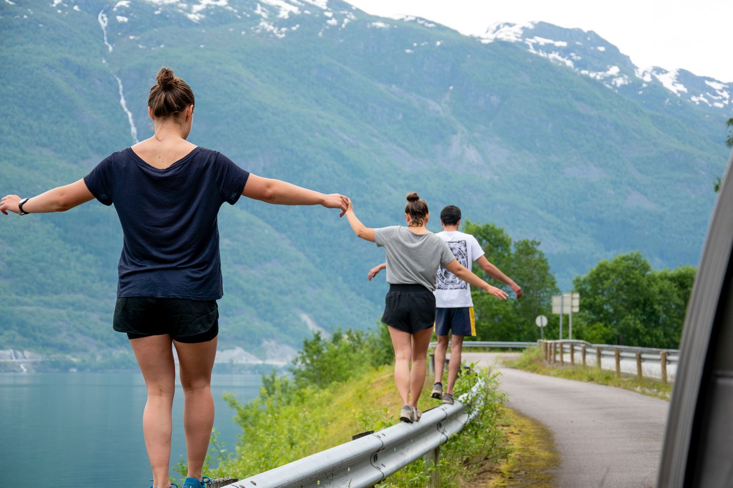 people balancing on a guardrail along the road in norway