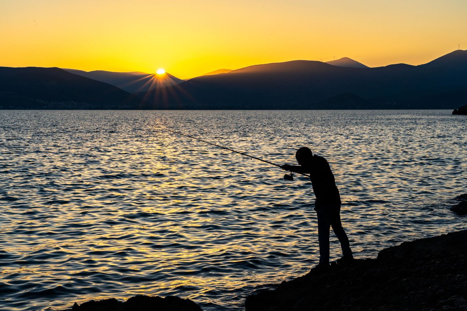 man fishing at sunset in greece
