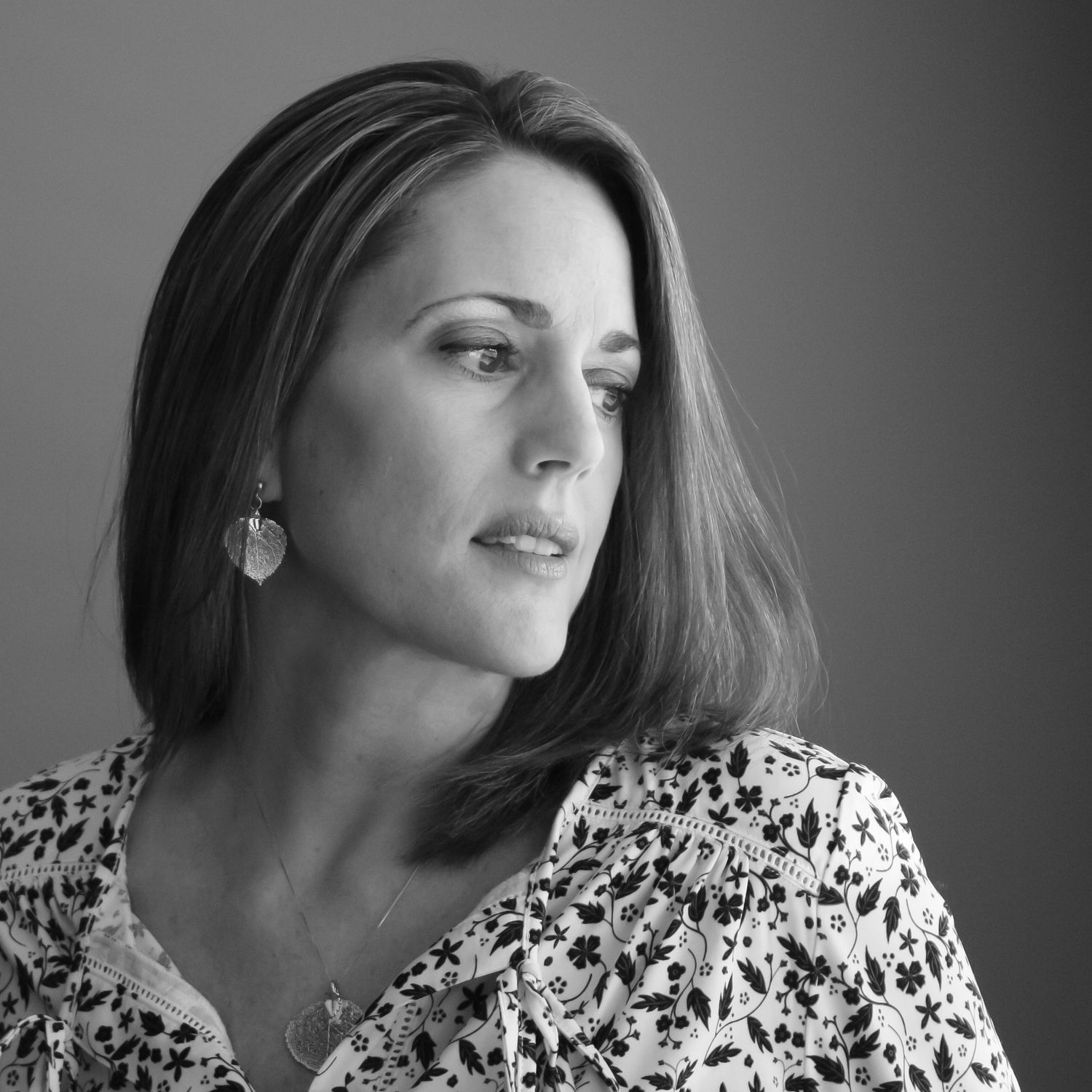 Black and white portrait of a woman with shoulder-length hair wearing floral blouse and earrings, gazing thoughtfully.