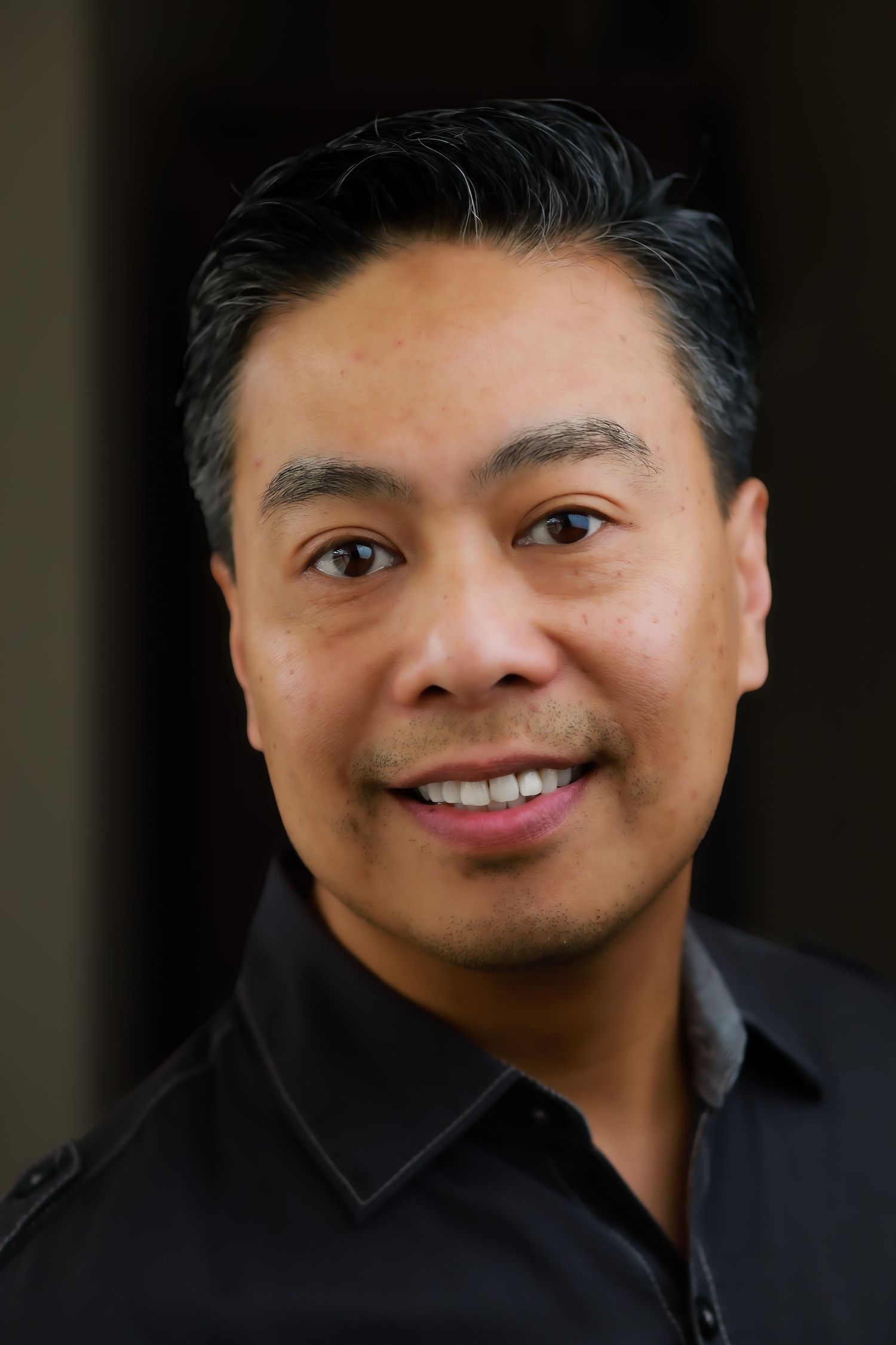 Smiling man with dark hair wearing a black shirt, professional headshot portrait.
