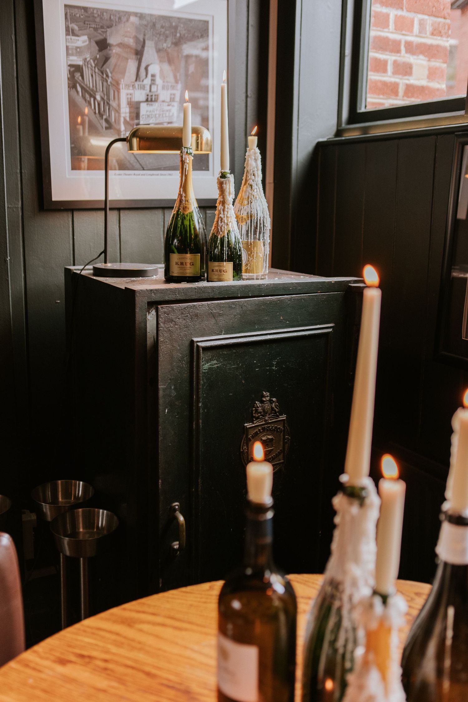 Rustic wooden table with wine bottles and candlesticks in a cozy brick-walled restaurant interior.