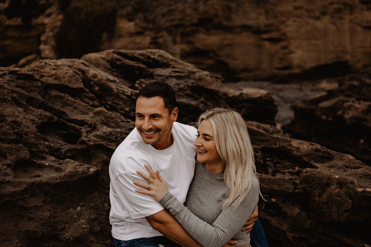 A couple shares a joyful moment together while sitting on rocky terrain at sunset.