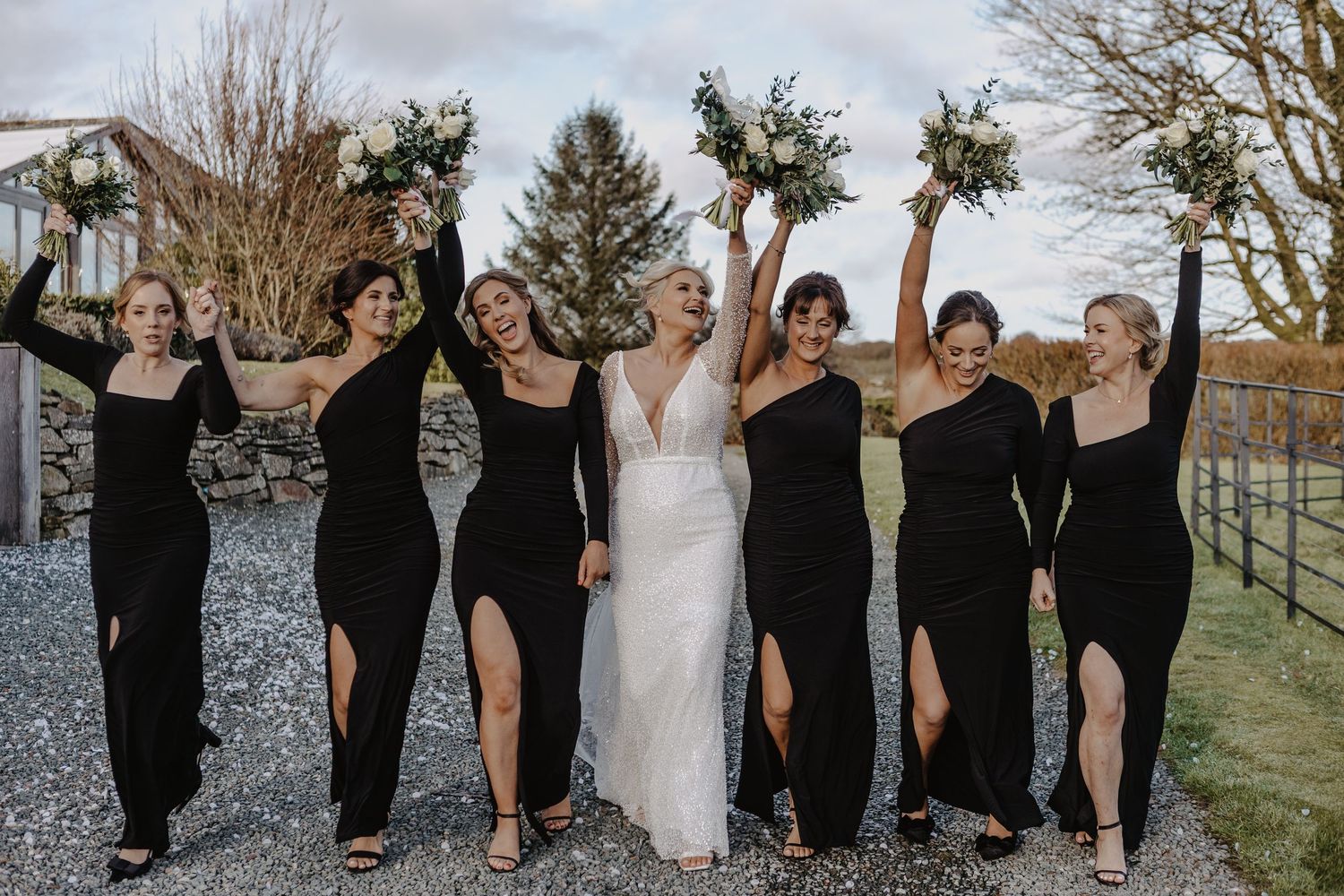Bridal party in black and white attire poses together on a rustic path during fall season.