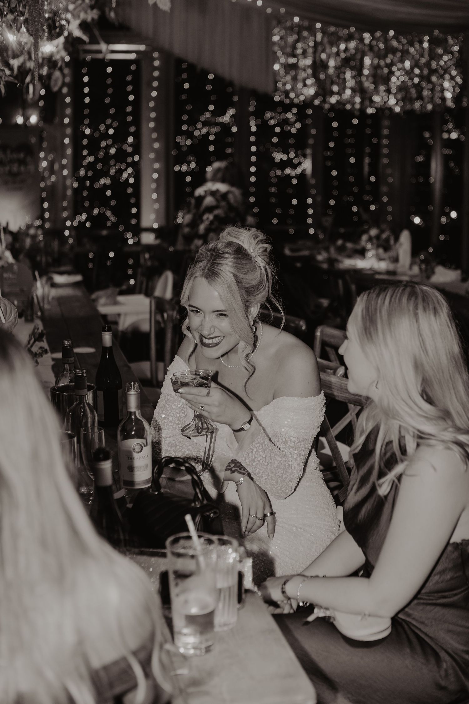 A candid black and white photo captures a joyful moment of laughter at a social gathering with twinkling lights in background.
