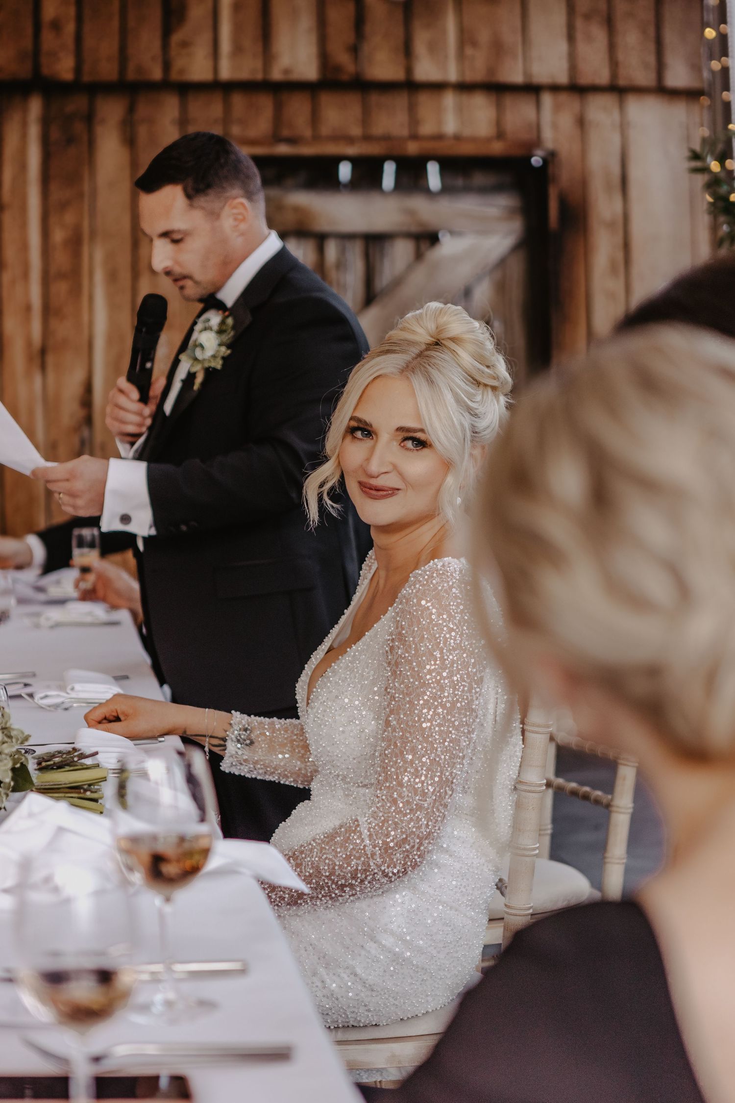 Elegant wedding reception in rustic barn venue with sparkly sequined dress and formal table settings.