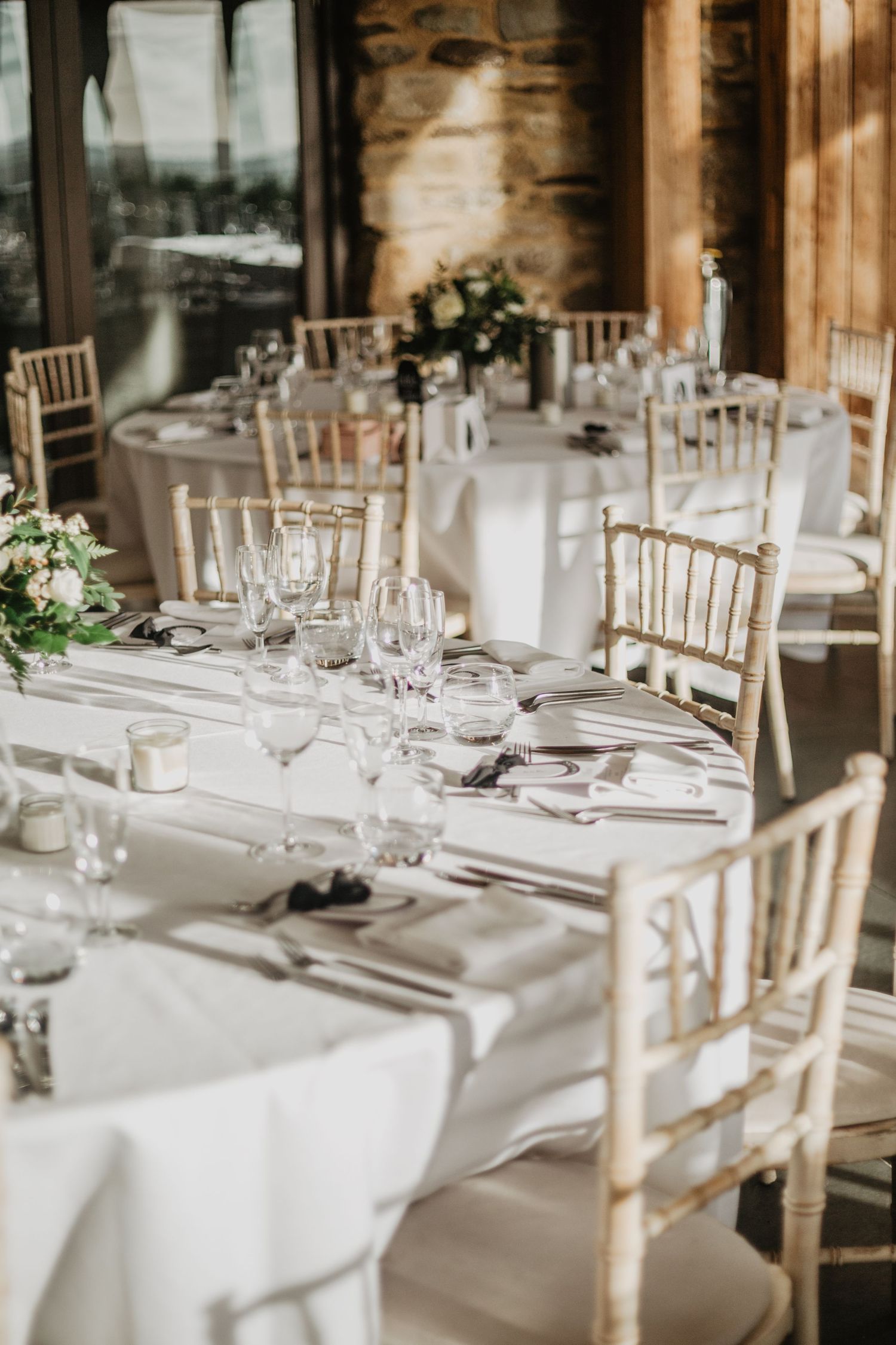 Elegant wedding reception tables set with white linens, gold chiavari chairs, and delicate floral centerpieces.