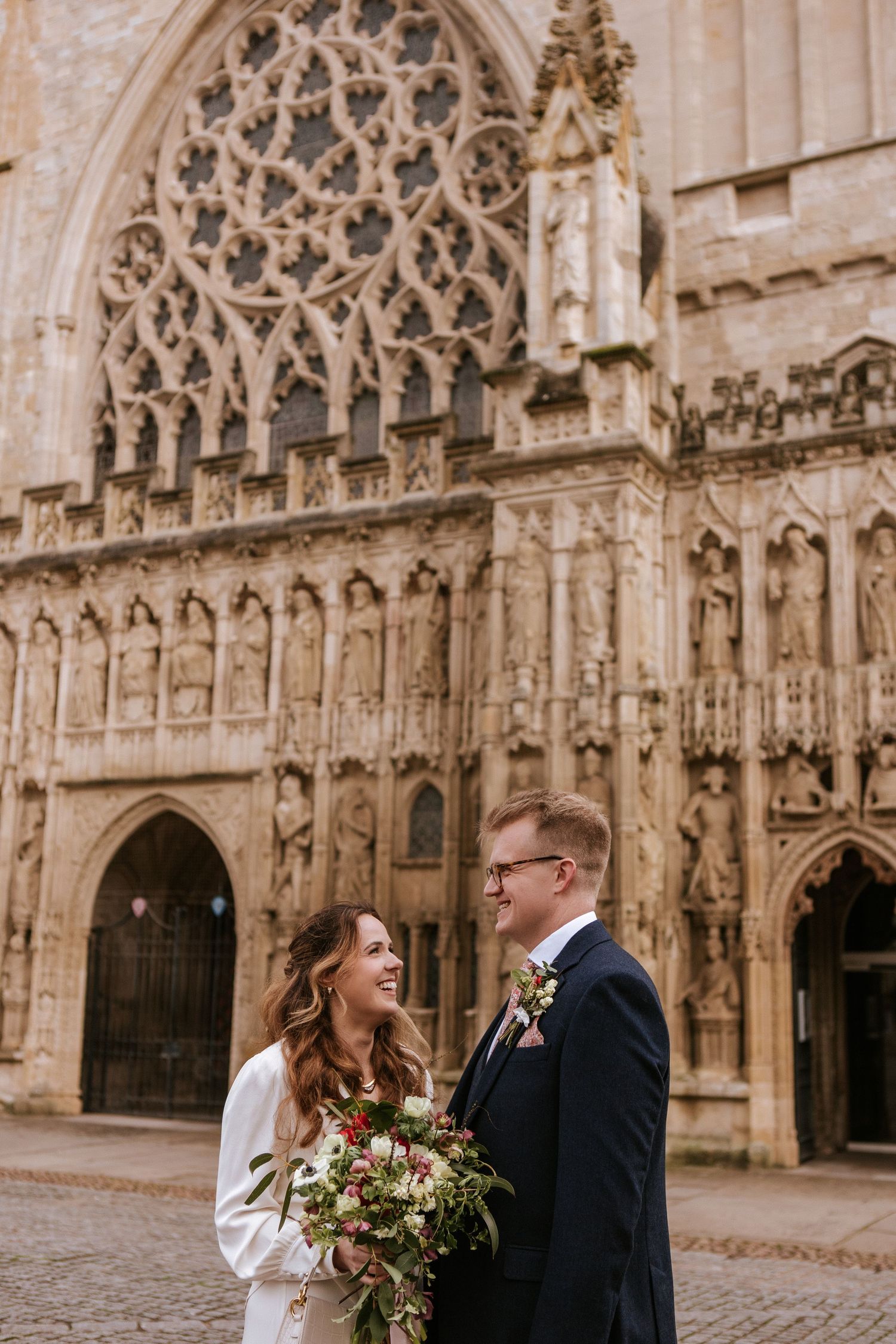 A couple shares a romantic moment in front of an ornate Gothic cathedral with intricate stone carvings and architecture.