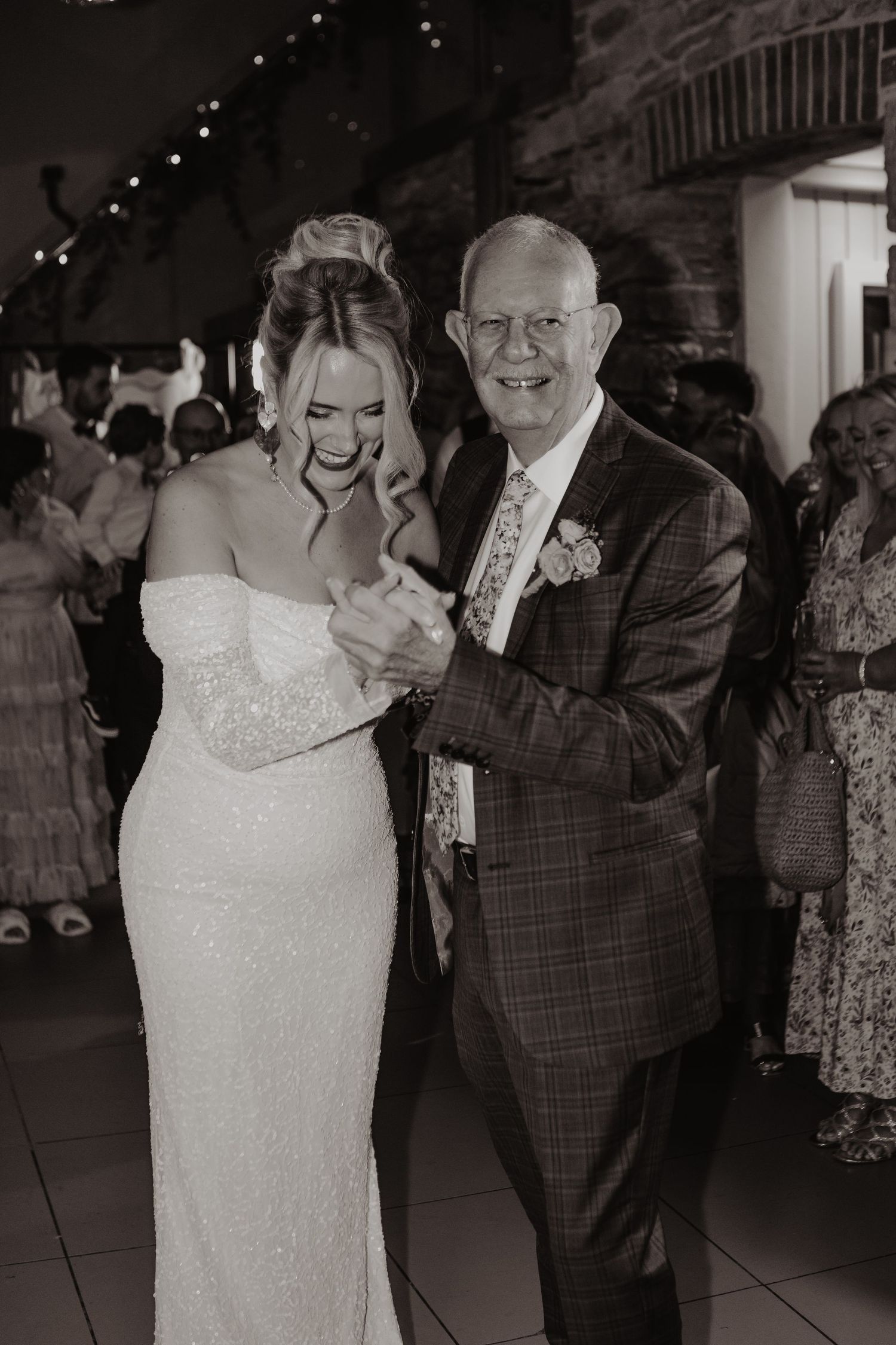 A couple shares a tender dance moment at a wedding reception, with the bride in a white dress and groom in plaid suit.