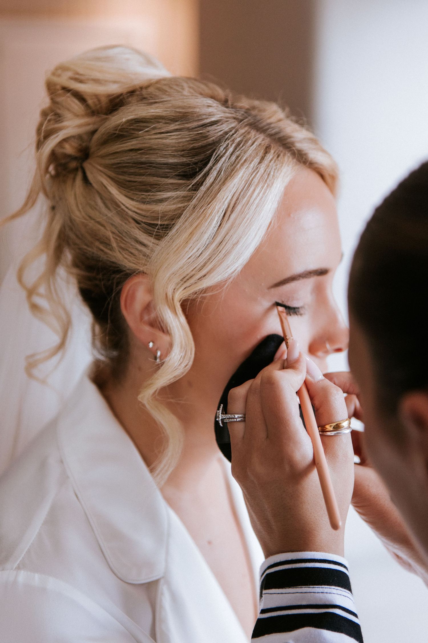 Professional makeup artist applies eye shadow to bride during wedding day preparation.