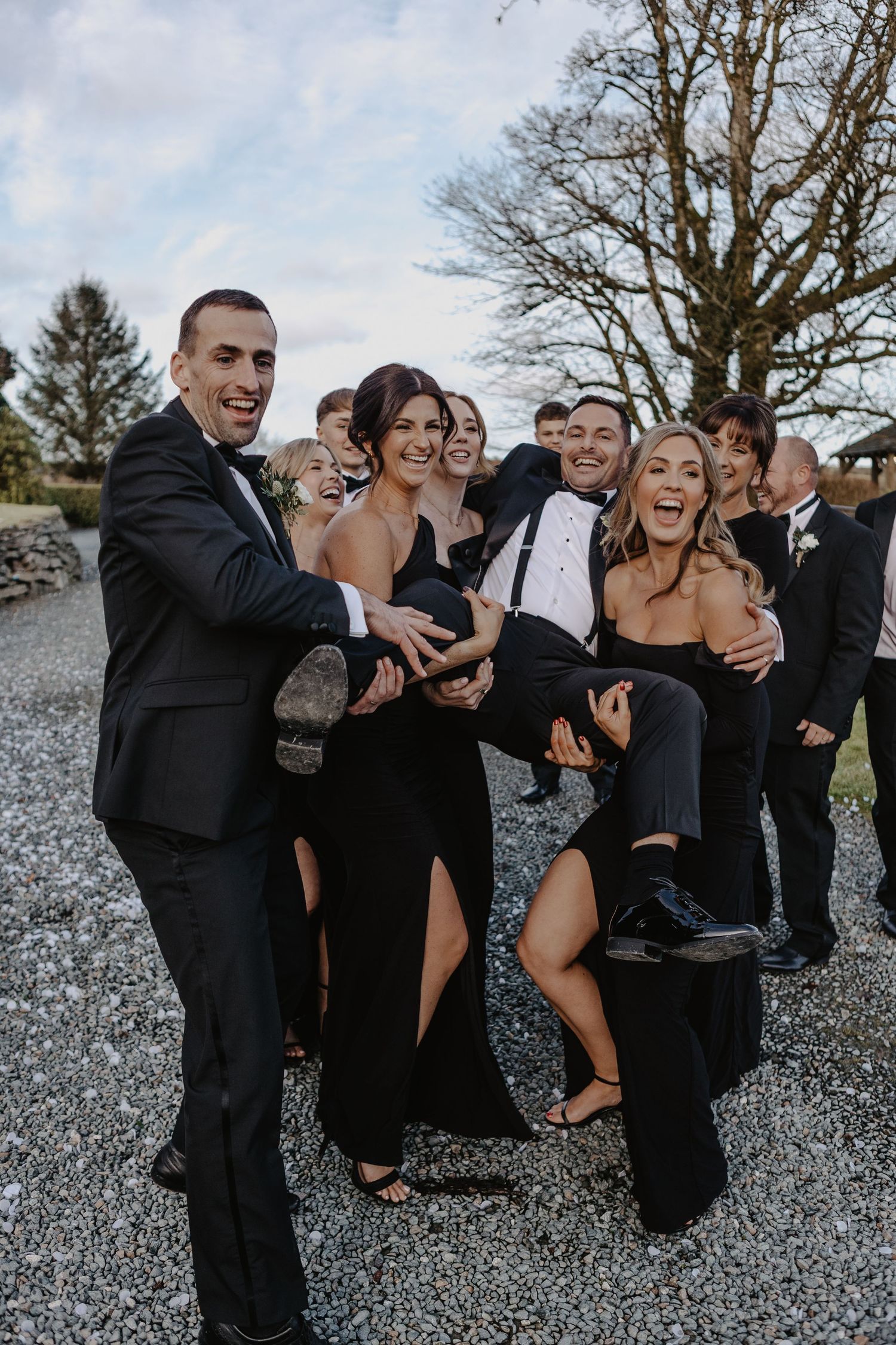 Wedding party in formal attire laughs together while posing on gravel ground in a candid photo sequence.