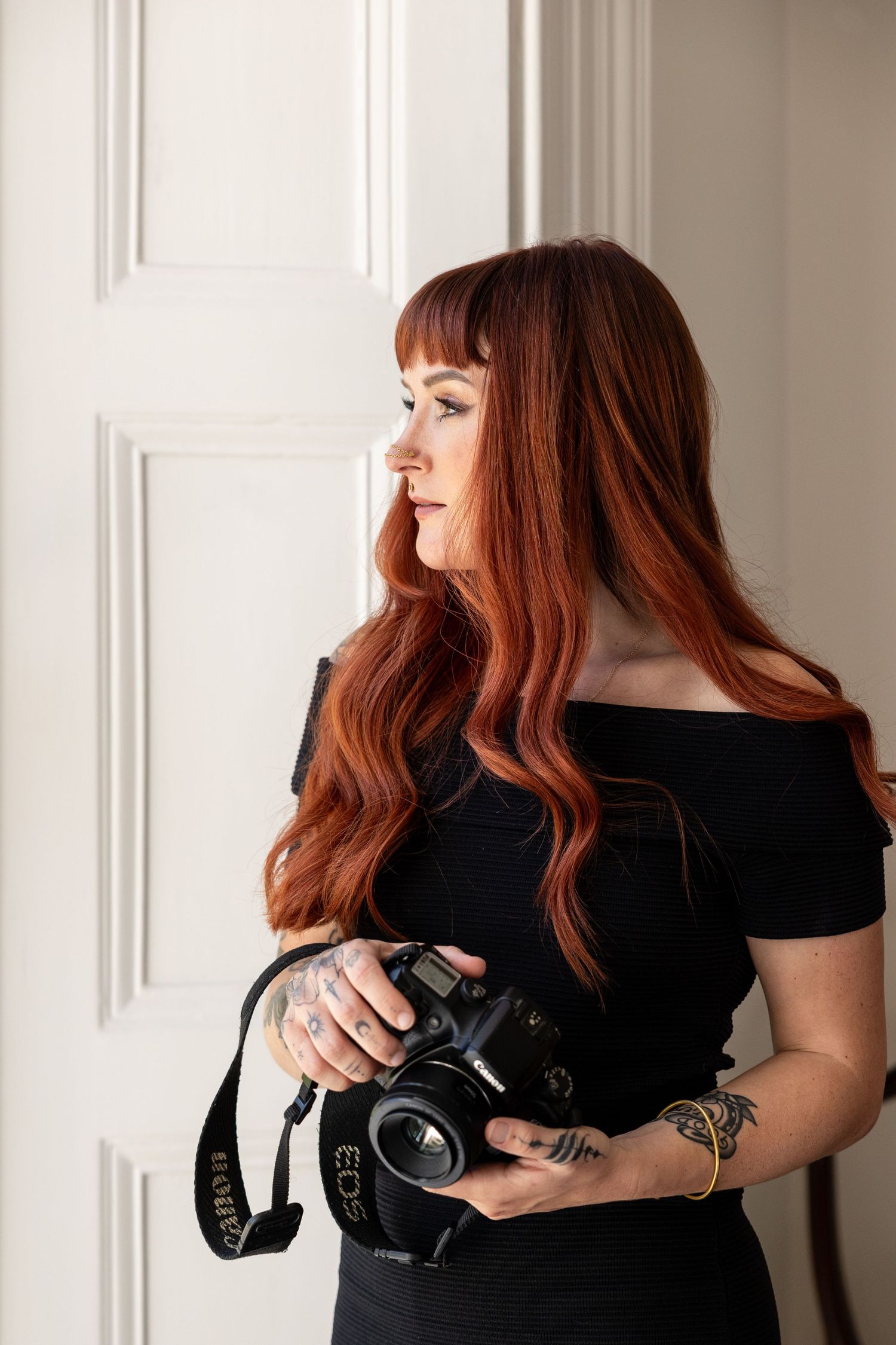 Portrait photographer with red hair holding professional camera in bright studio.