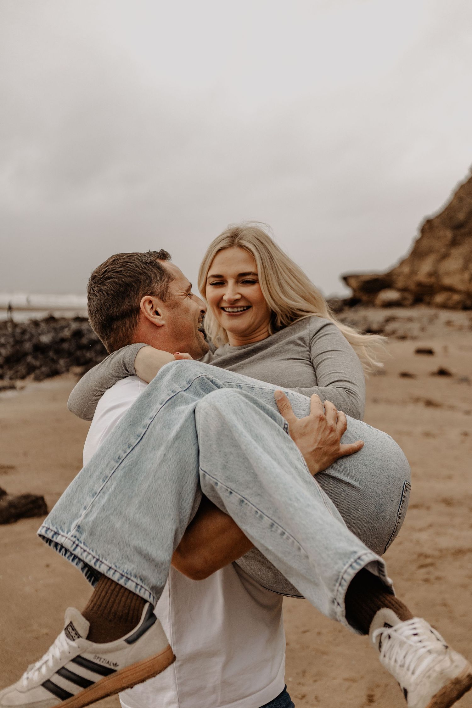 Joyful couple in casual attire playing and laughing on coastal beach.