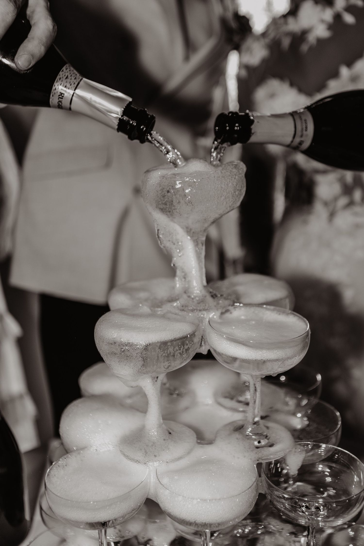 Champagne being poured into a tower of elegant coupe glasses stacked in a pyramid formation at a celebration event.