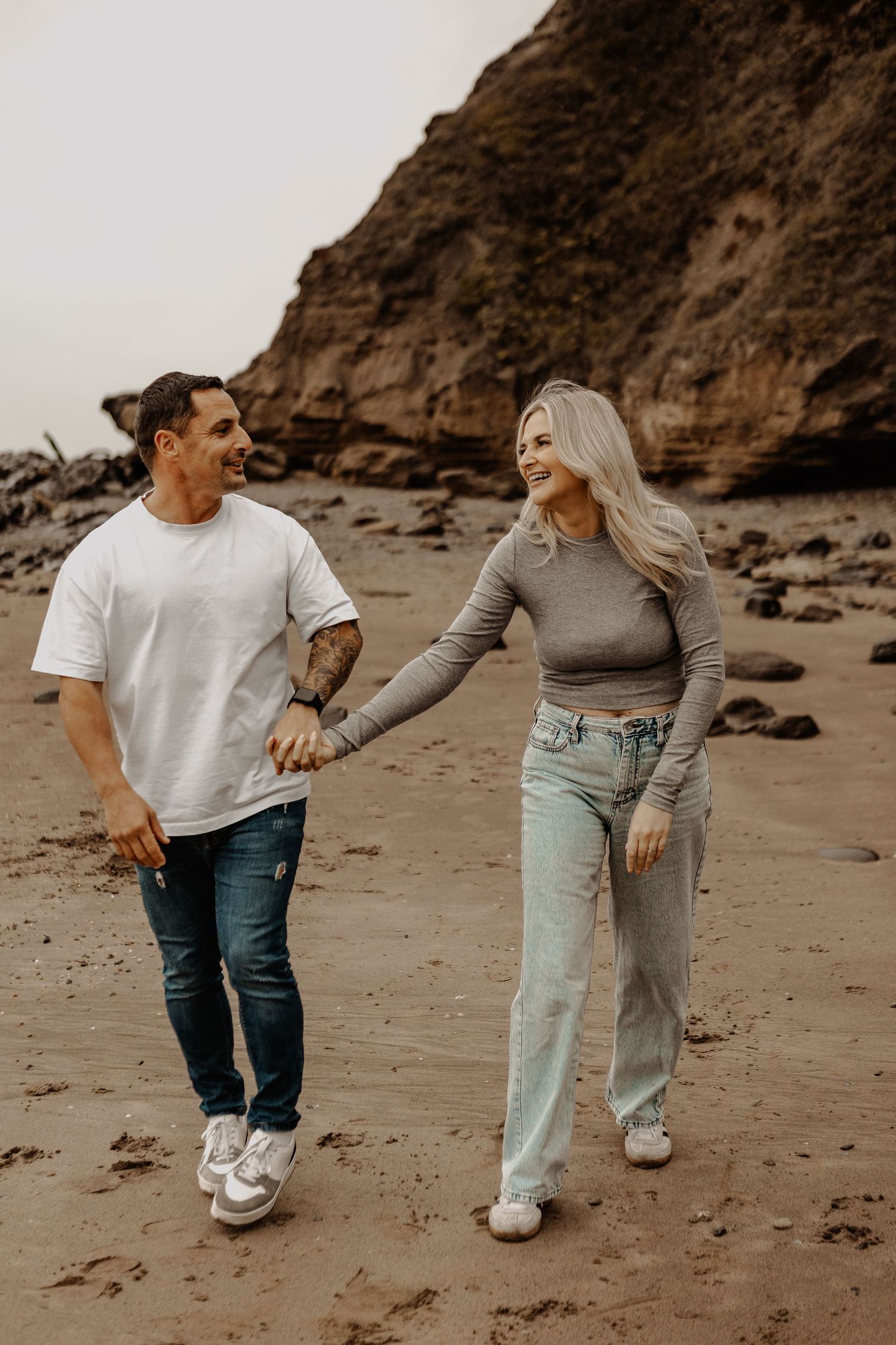 Playful couple in casual wear walking together on sandy beach.