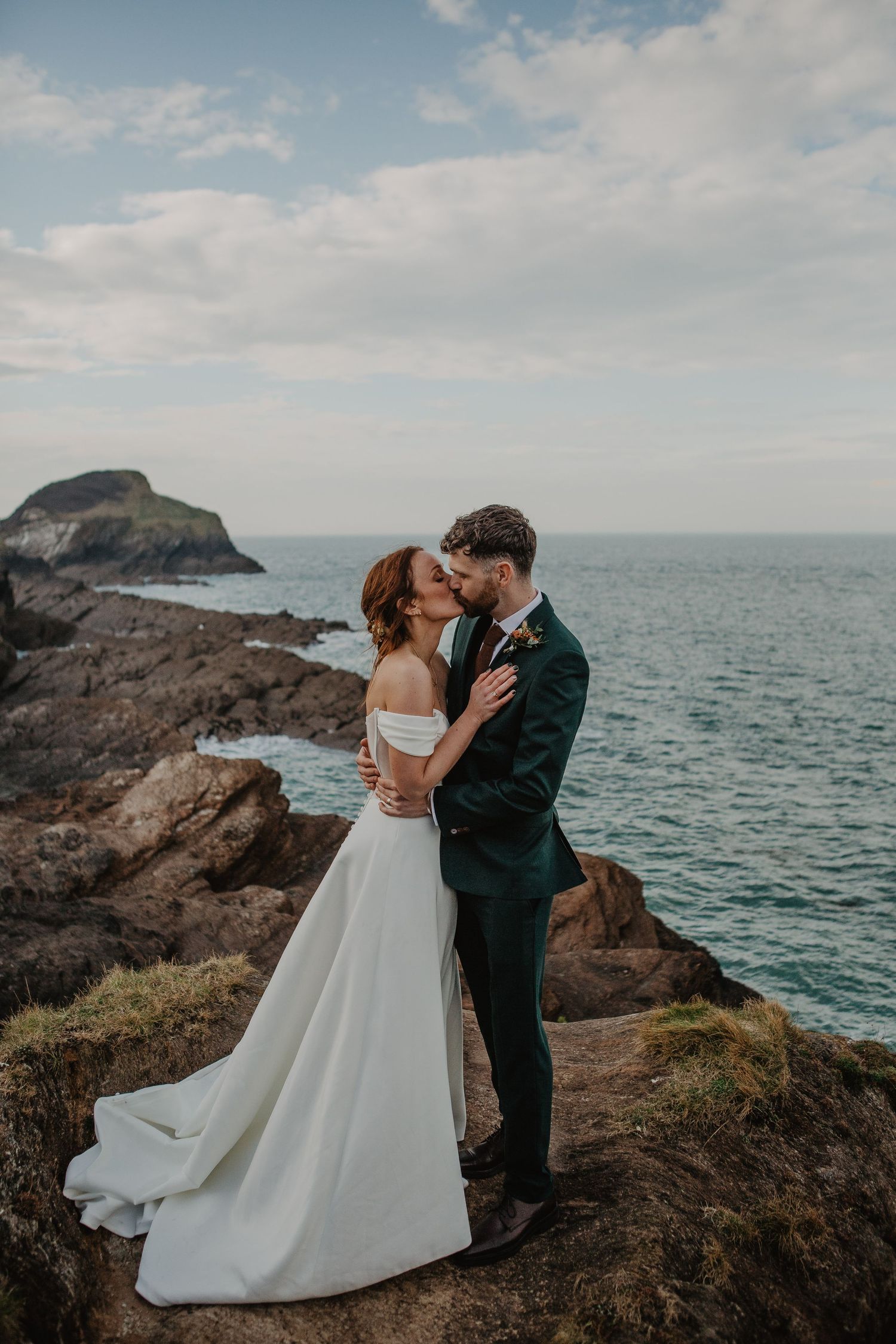 Romantic wedding couple embraces on dramatic coastal cliffs overlooking the ocean.