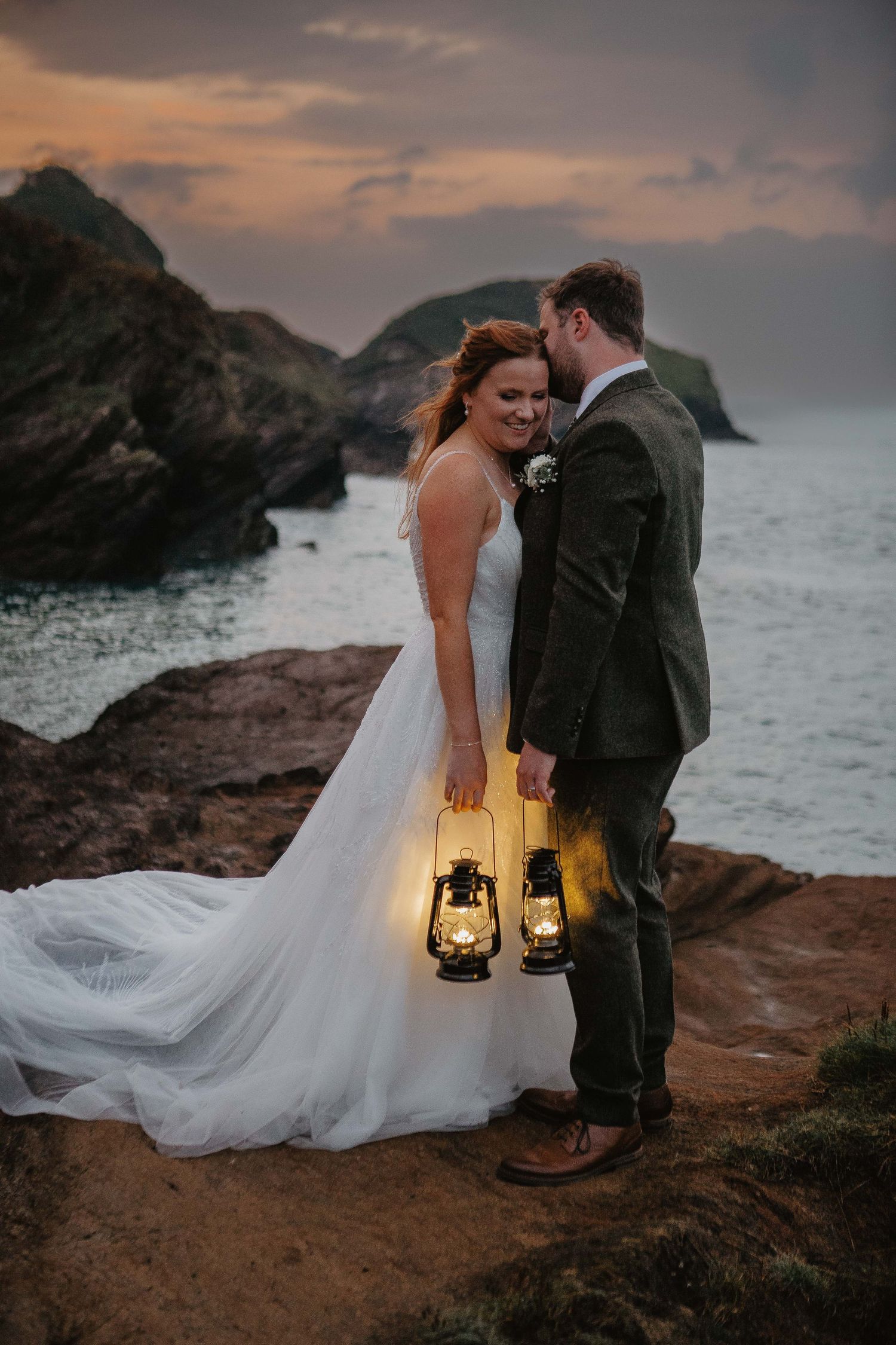 A romantic coastal wedding scene with lanterns glowing at sunset on rocky cliffs by the ocean.