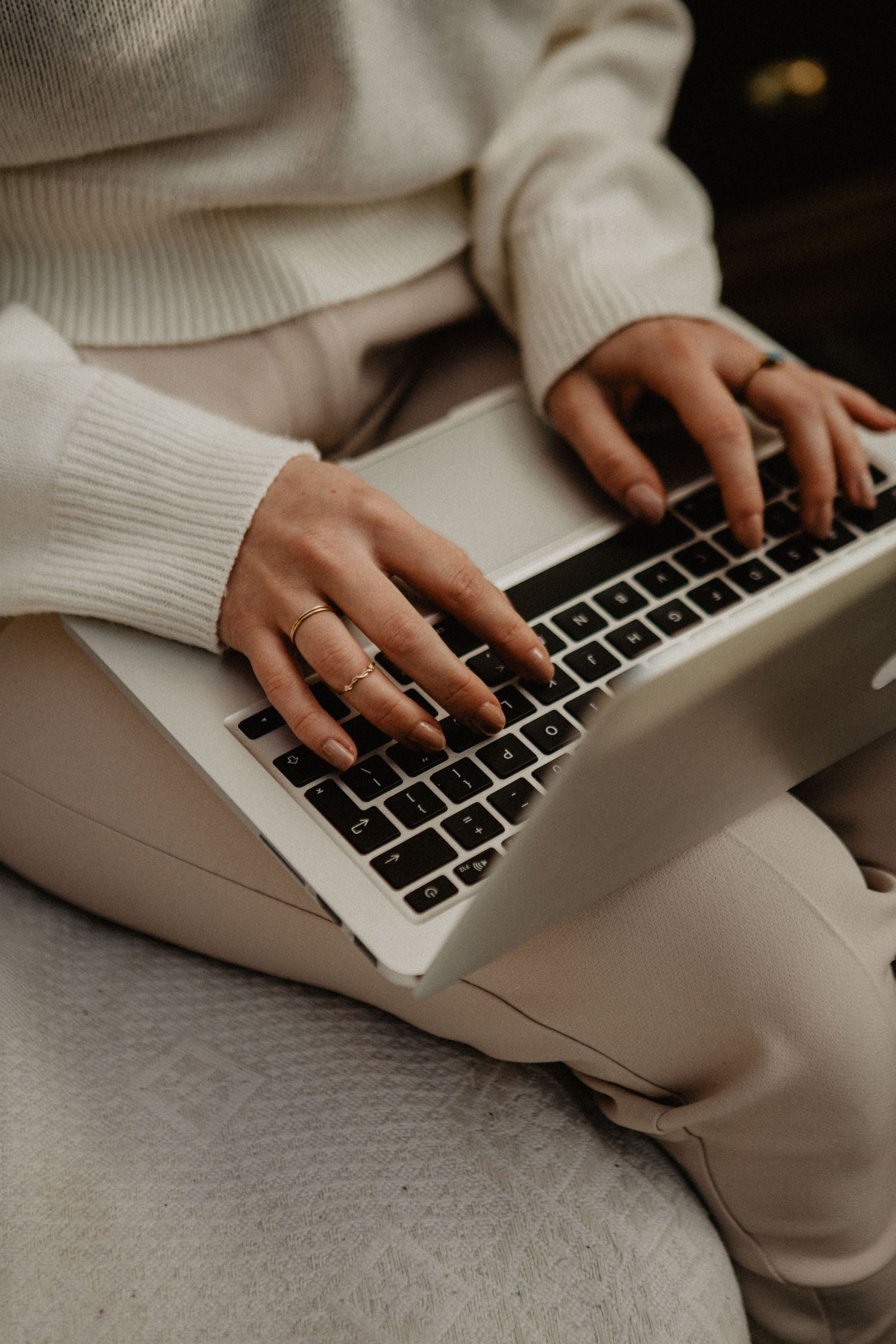 Close-up view of hands typing on a silver laptop keyboard while wearing a cozy cream sweater.
