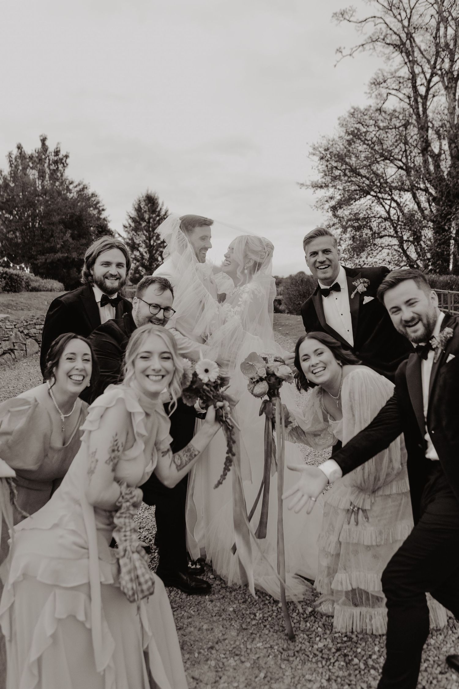 A group of people in formal attire pose together outdoors in a candid celebratory moment.