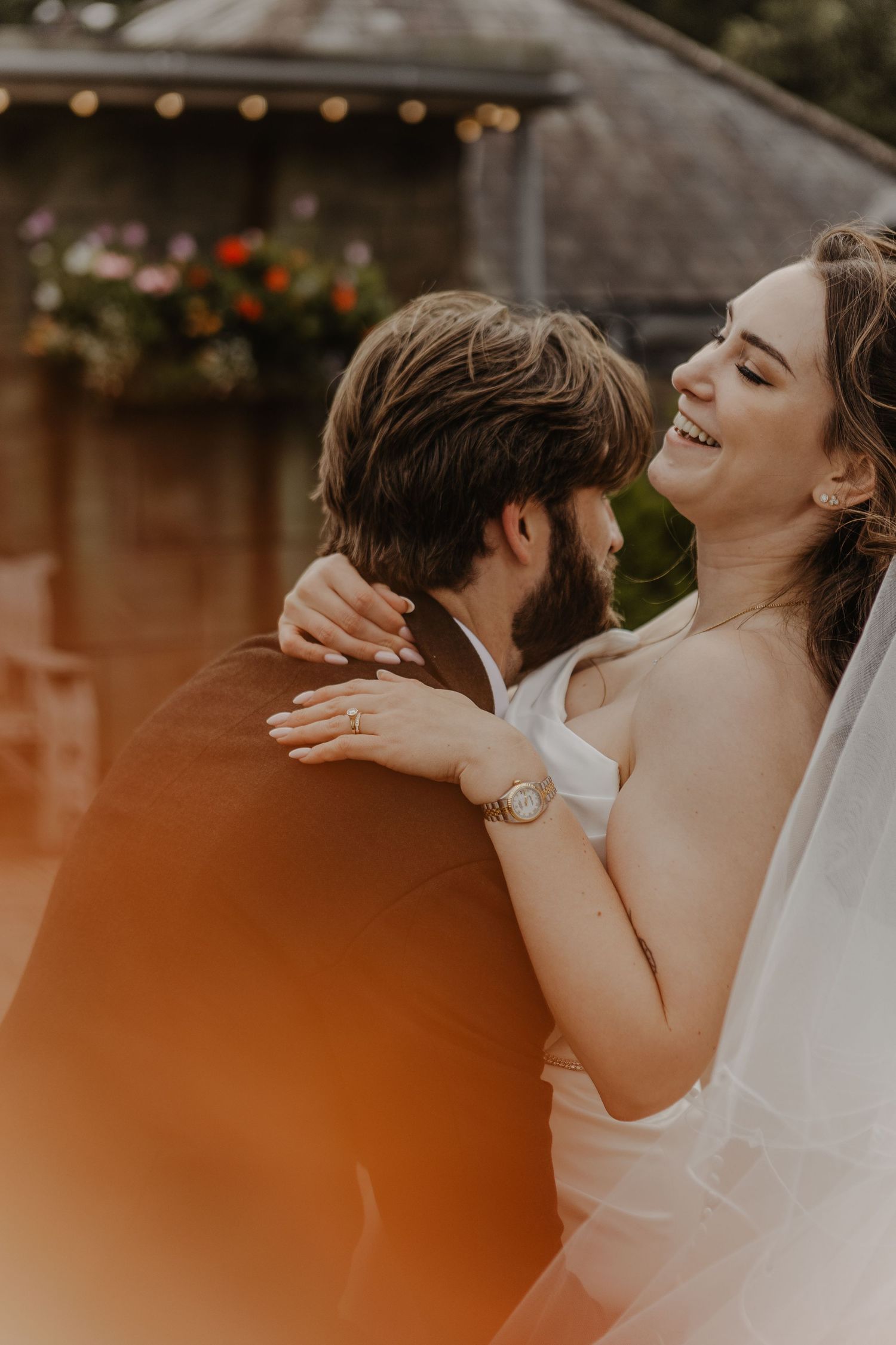 Intimate outdoor wedding moment with bride in white dress and veil embracing partner.