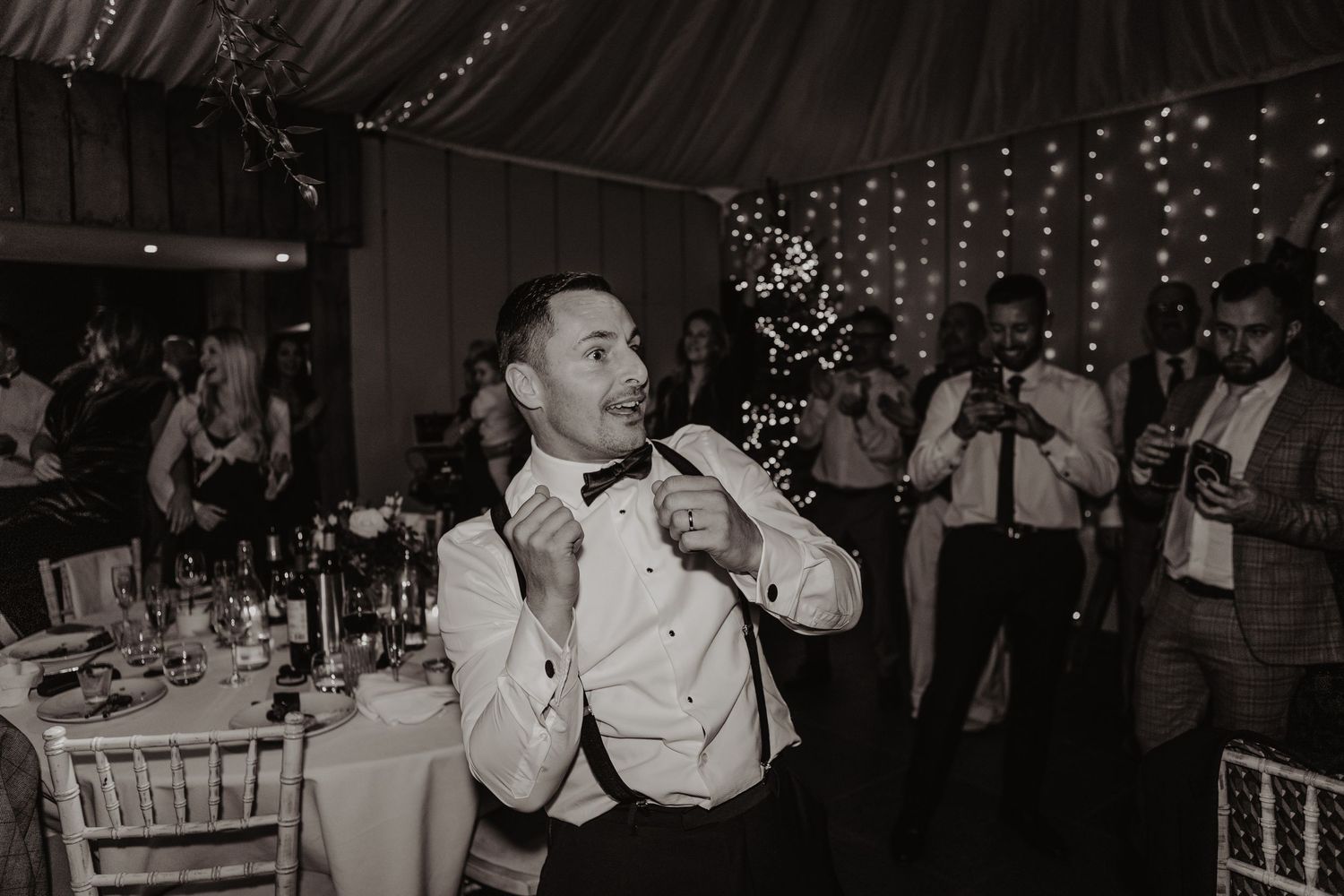 Guests dancing and celebrating at a wedding reception with twinkling lights and decorations in the background.