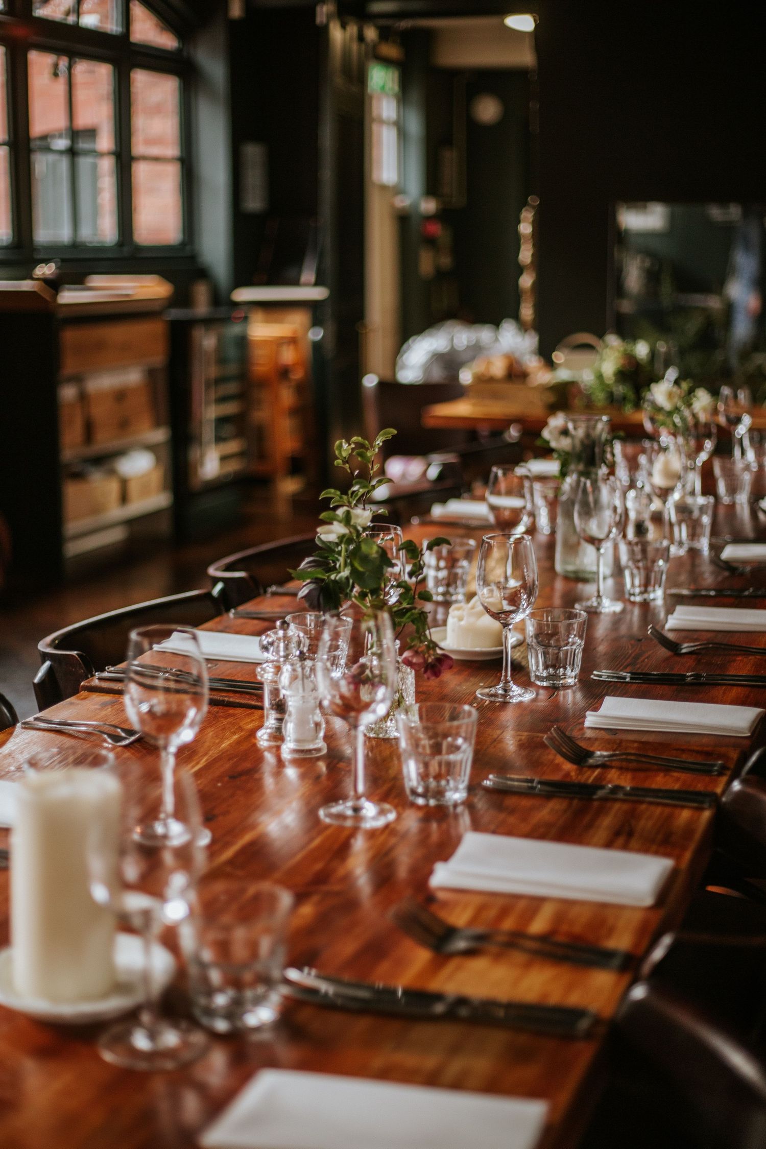 Elegant table setting with wine glasses and place settings on polished wooden table in a dimly lit restaurant interior.