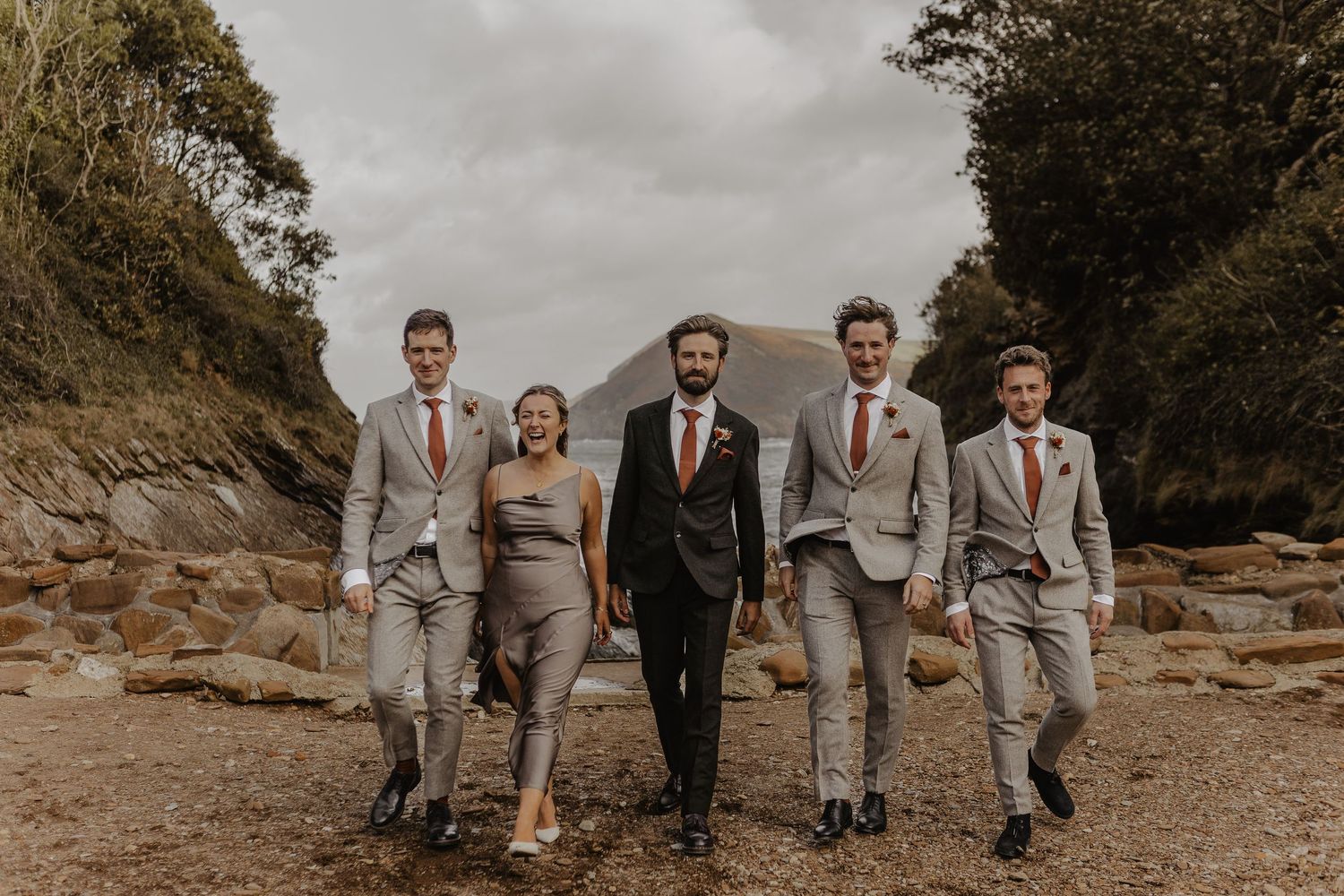 Wedding party in gray and black attire walking together on a scenic coastal path.