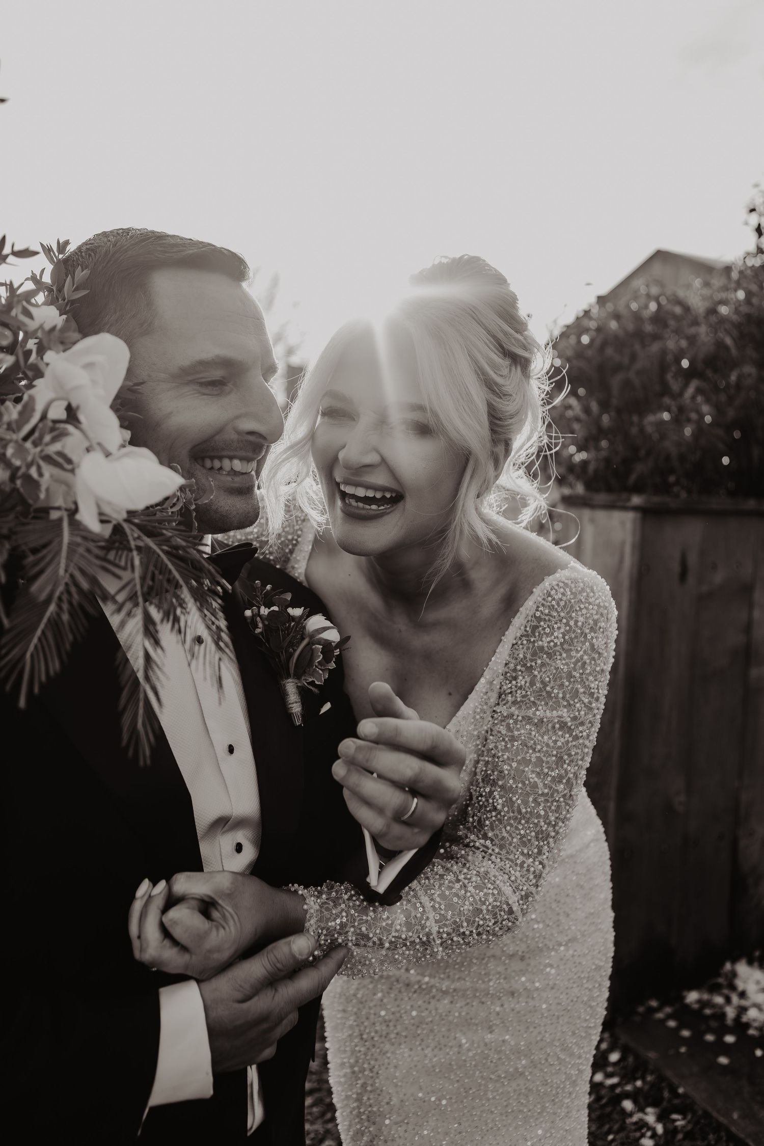 A joyful couple shares a candid moment together in black and white, with sunlight streaming behind them.