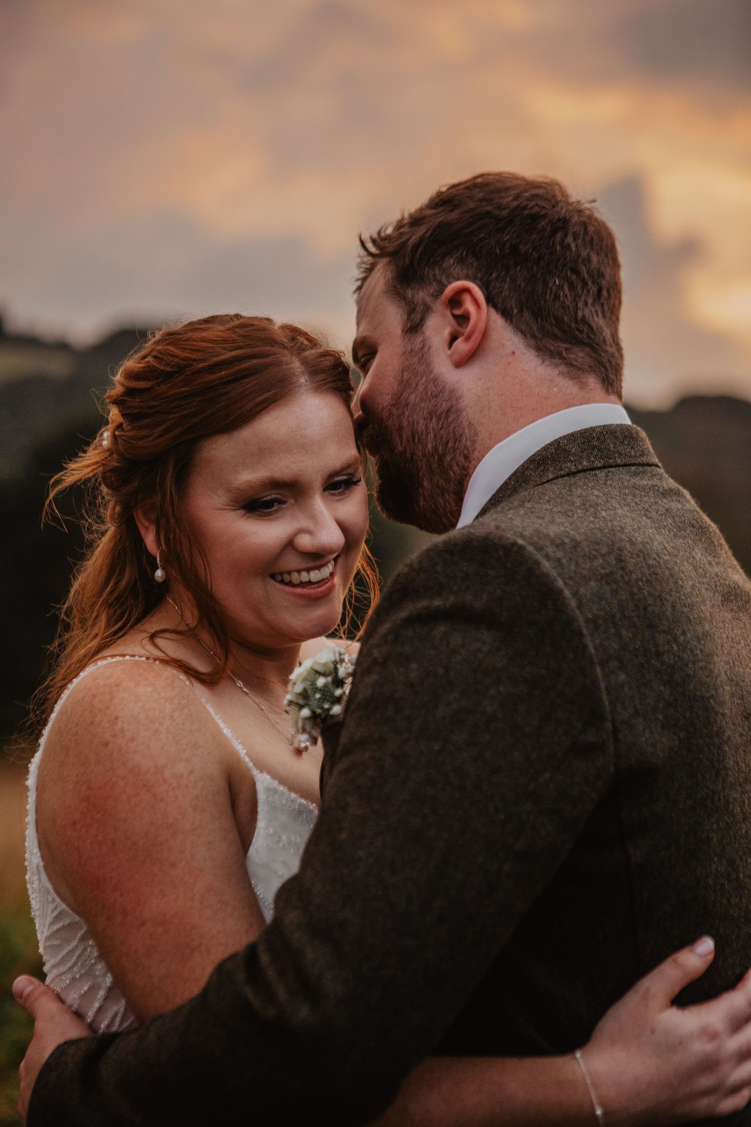 A tender wedding moment captured during golden hour with a couple embracing on a coastal cliff.