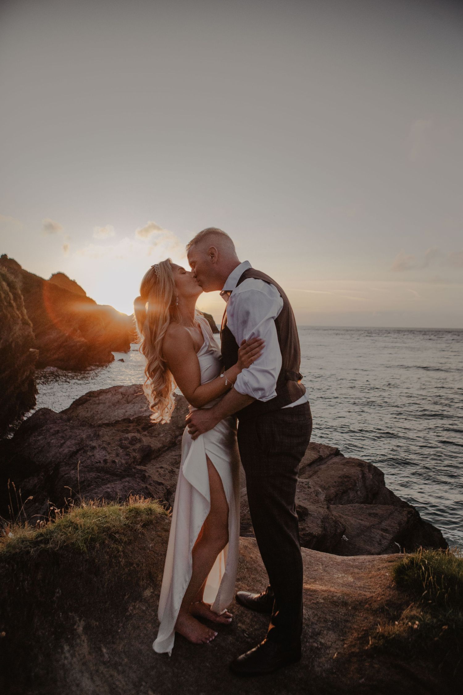 A romantic sunset moment captured on coastal rocks with ocean waves and golden light in the background.