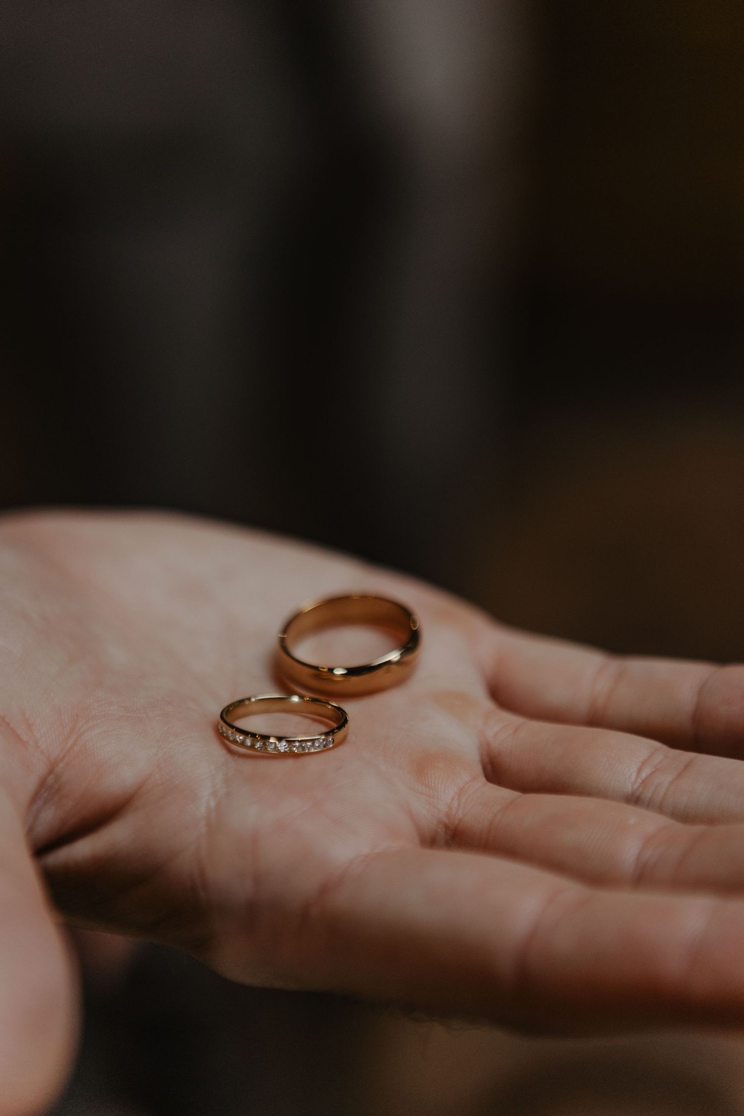 Two gold wedding rings resting in an open palm with one band featuring delicate diamond accents.