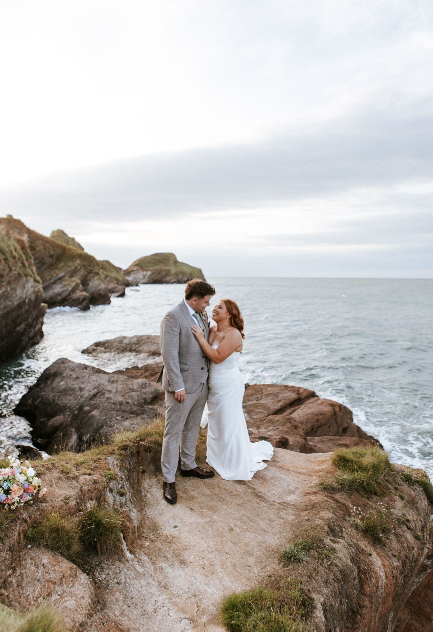 A couple shares a romantic moment on a dramatic coastal cliff overlooking the ocean in five sequential photographs.