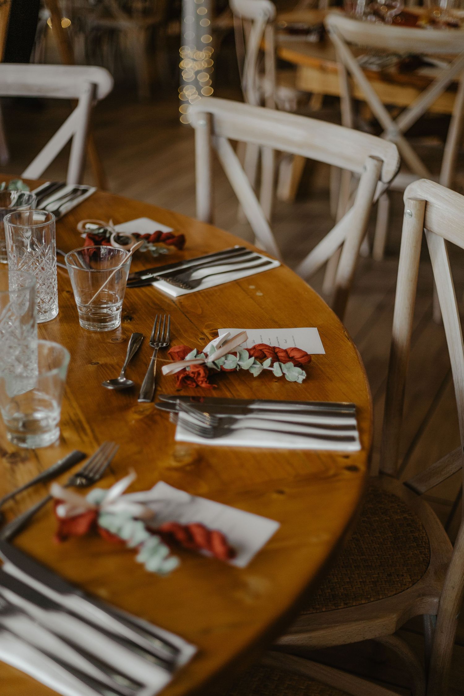 Elegant table setting with crystal glasses and white chairs at rustic wedding reception.