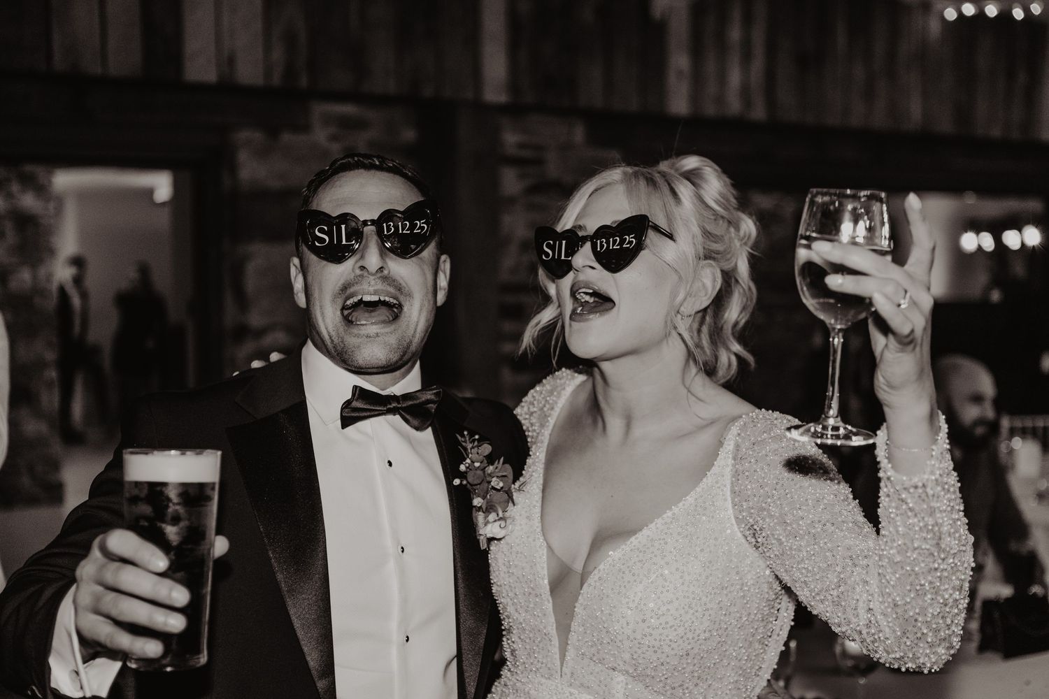 A group of formally dressed party guests wearing sunglasses and bow ties laugh and celebrate at an elegant event.