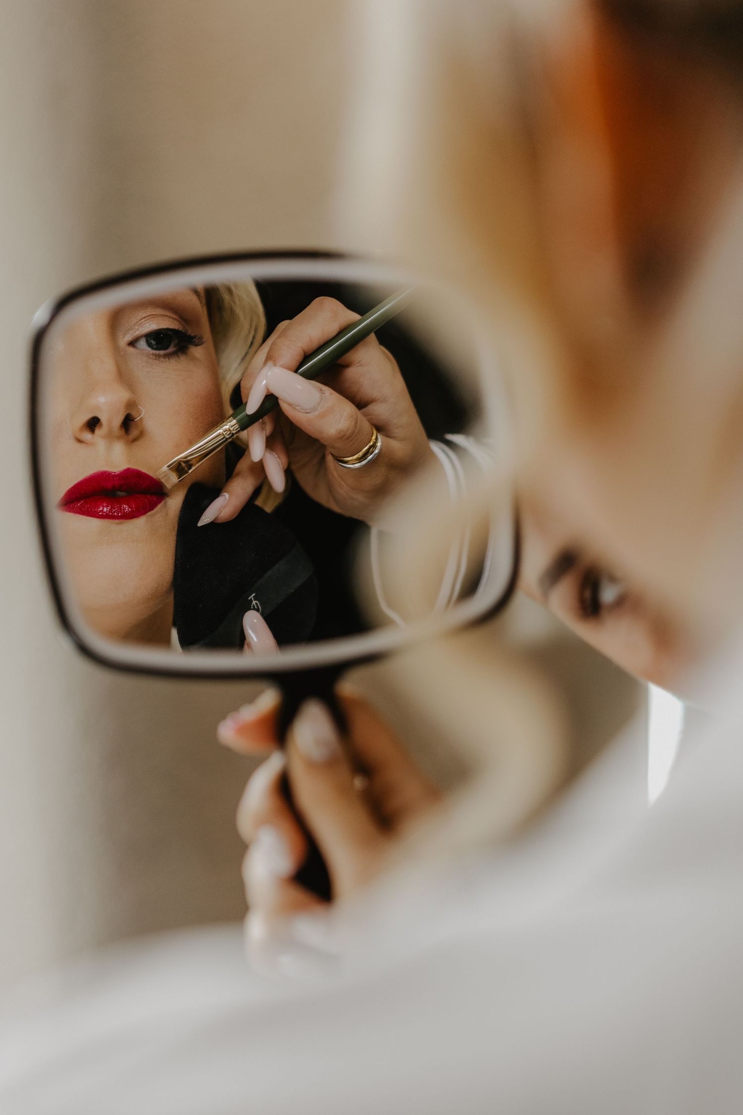 Close-up view of someone applying mascara while looking in a handheld mirror in soft natural lighting.