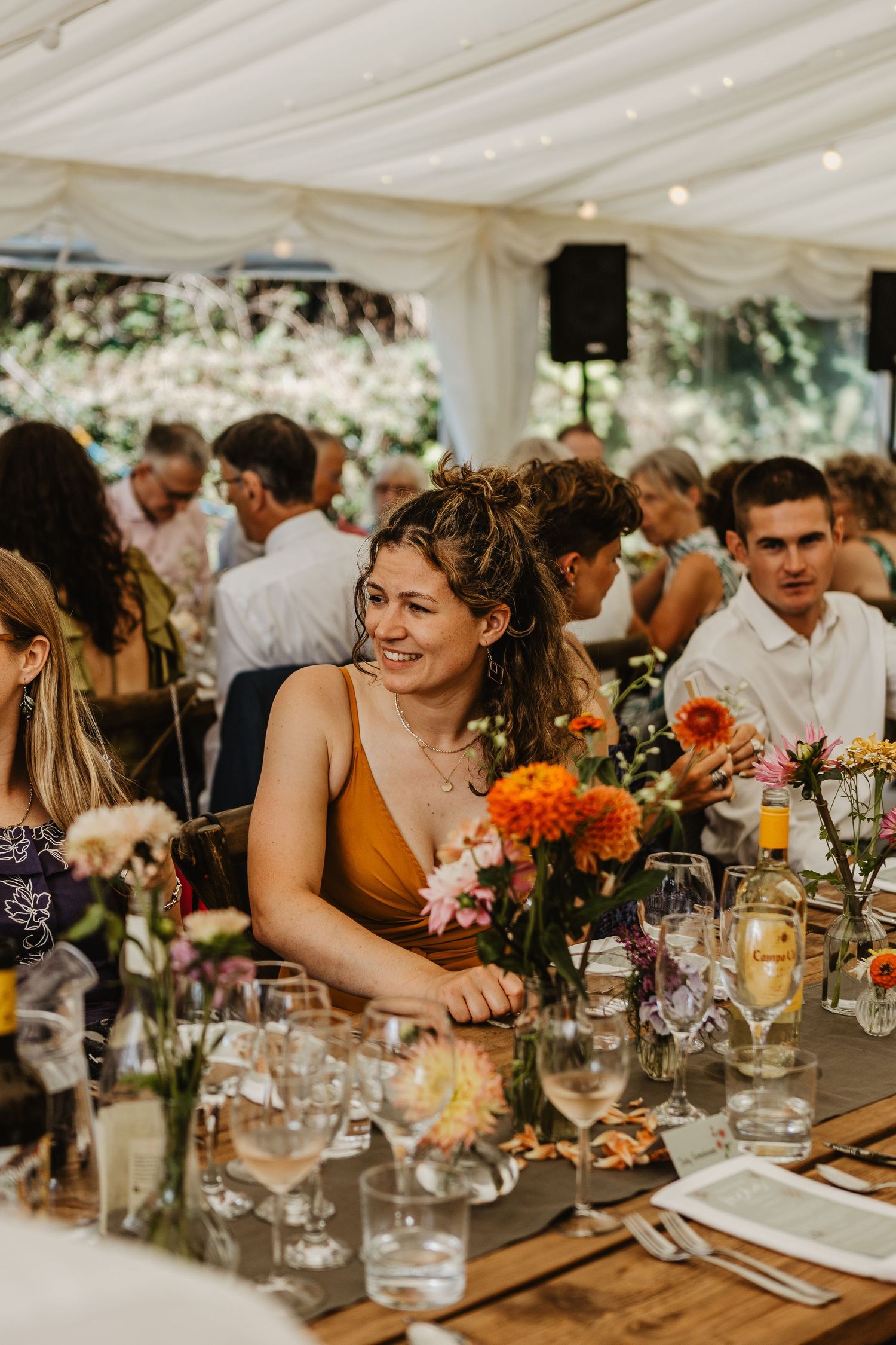 Wedding reception in a decorated marquee tent with floral centerpieces and happy guests.