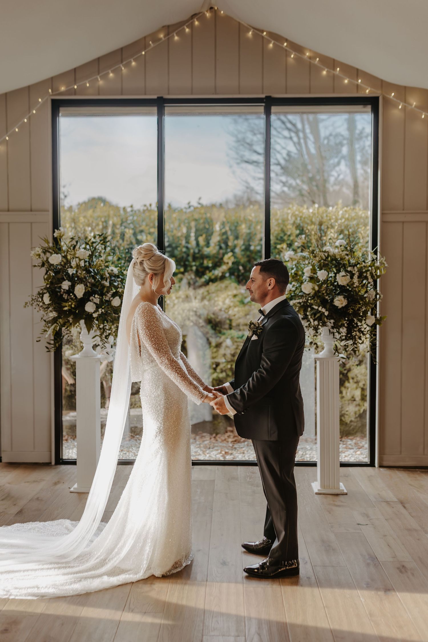 A couple shares their first look moment in a modern white wedding venue decorated with string lights and floral arrangements.