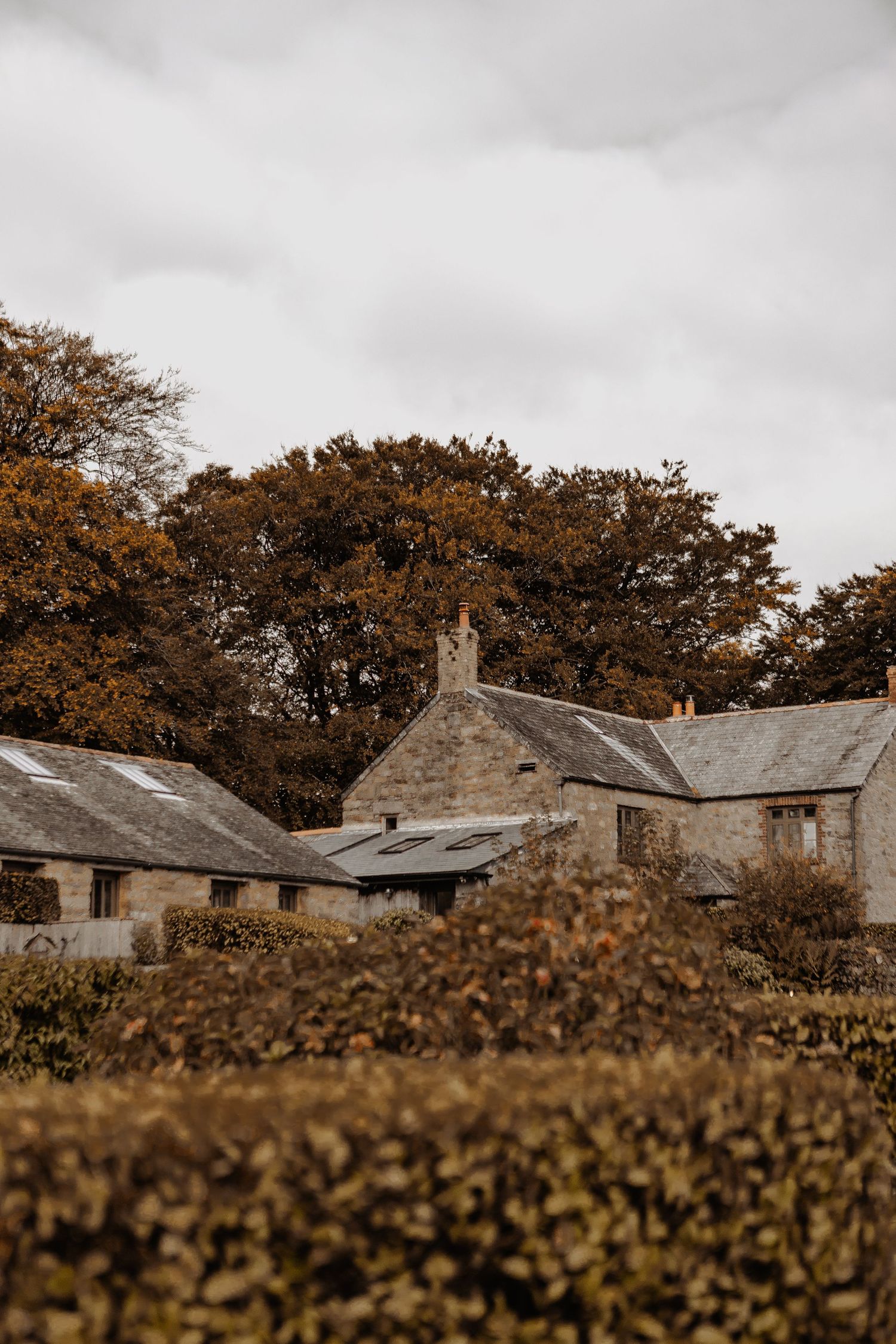 Stone cottages nestled among autumn trees under an overcast sky.