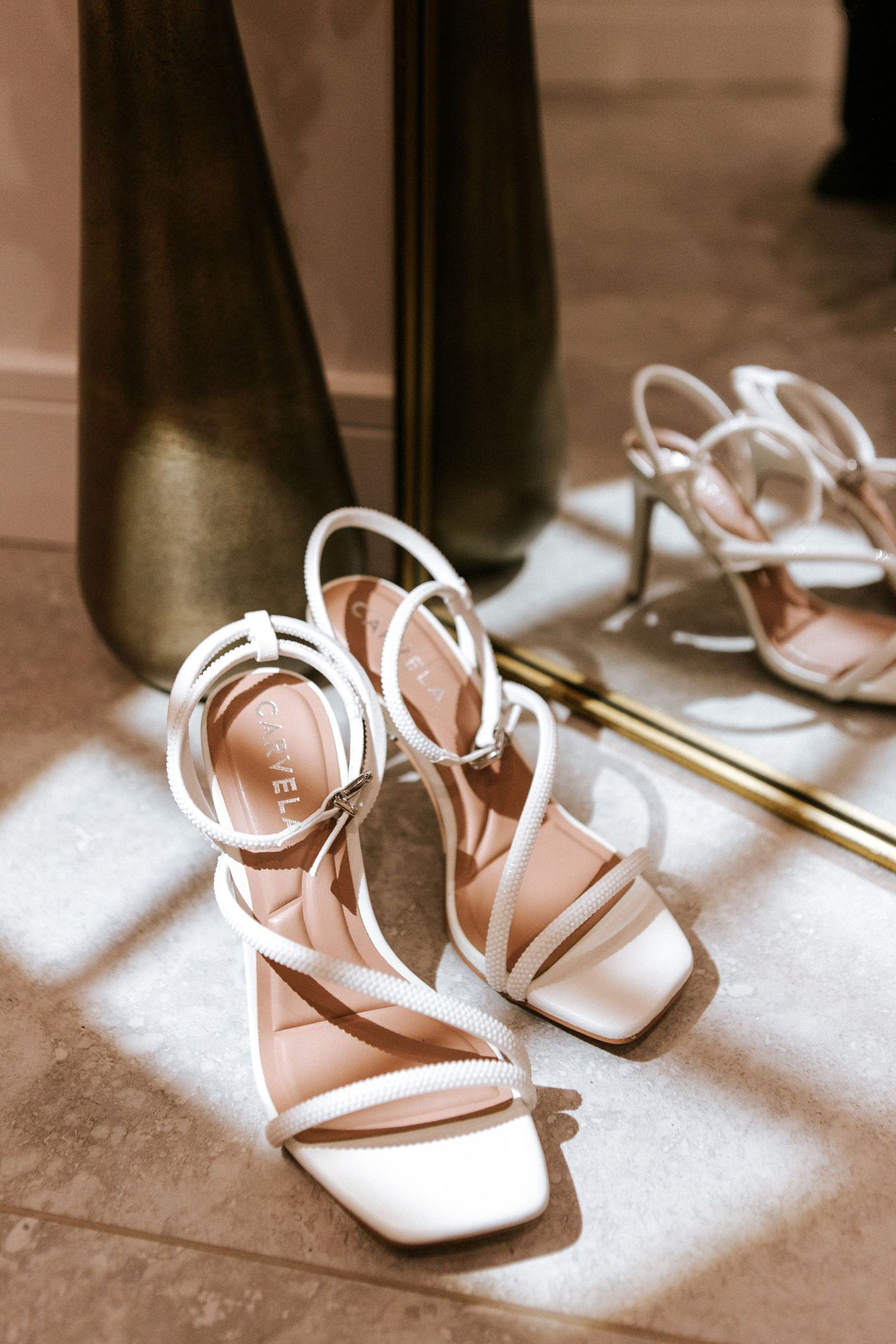 Elegant white strappy wedding sandals arranged in a row with dramatic shadows cast across a light surface.