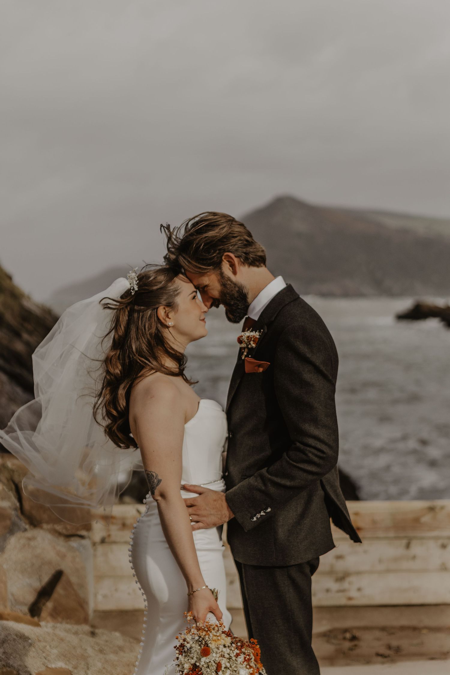 Couple shares an intimate moment on their wedding day against a moody coastal backdrop.