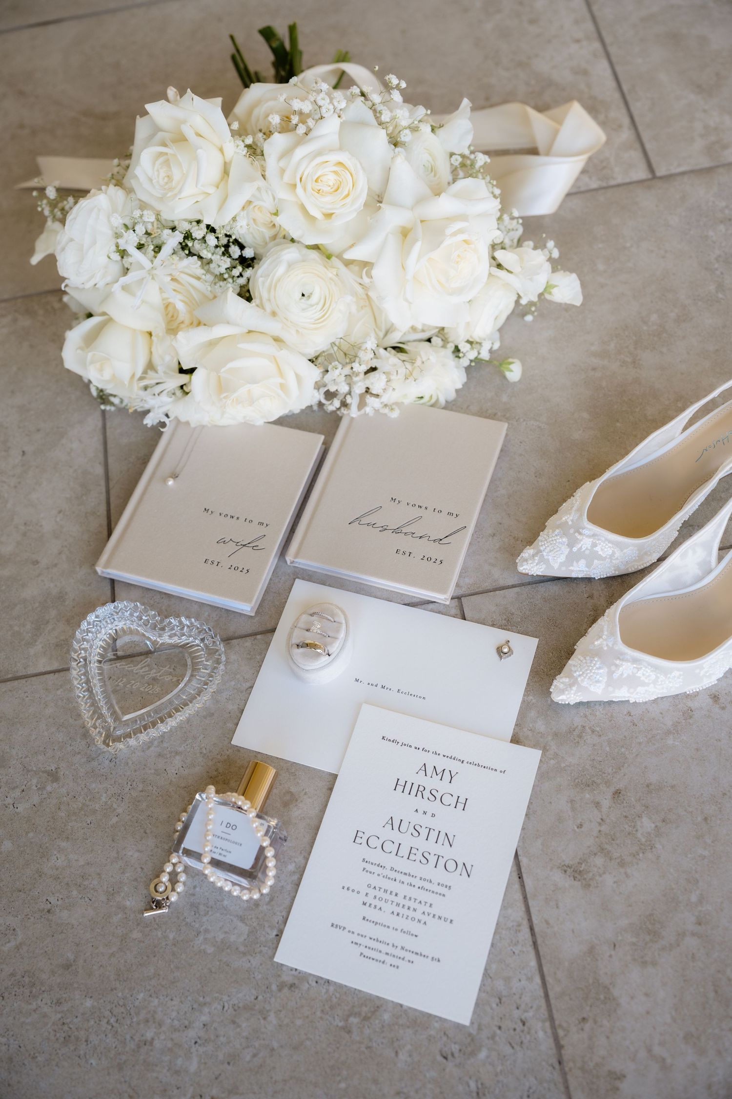 Wedding details flat lay with white roses, invitations, jewelry and shoes on stone floor.