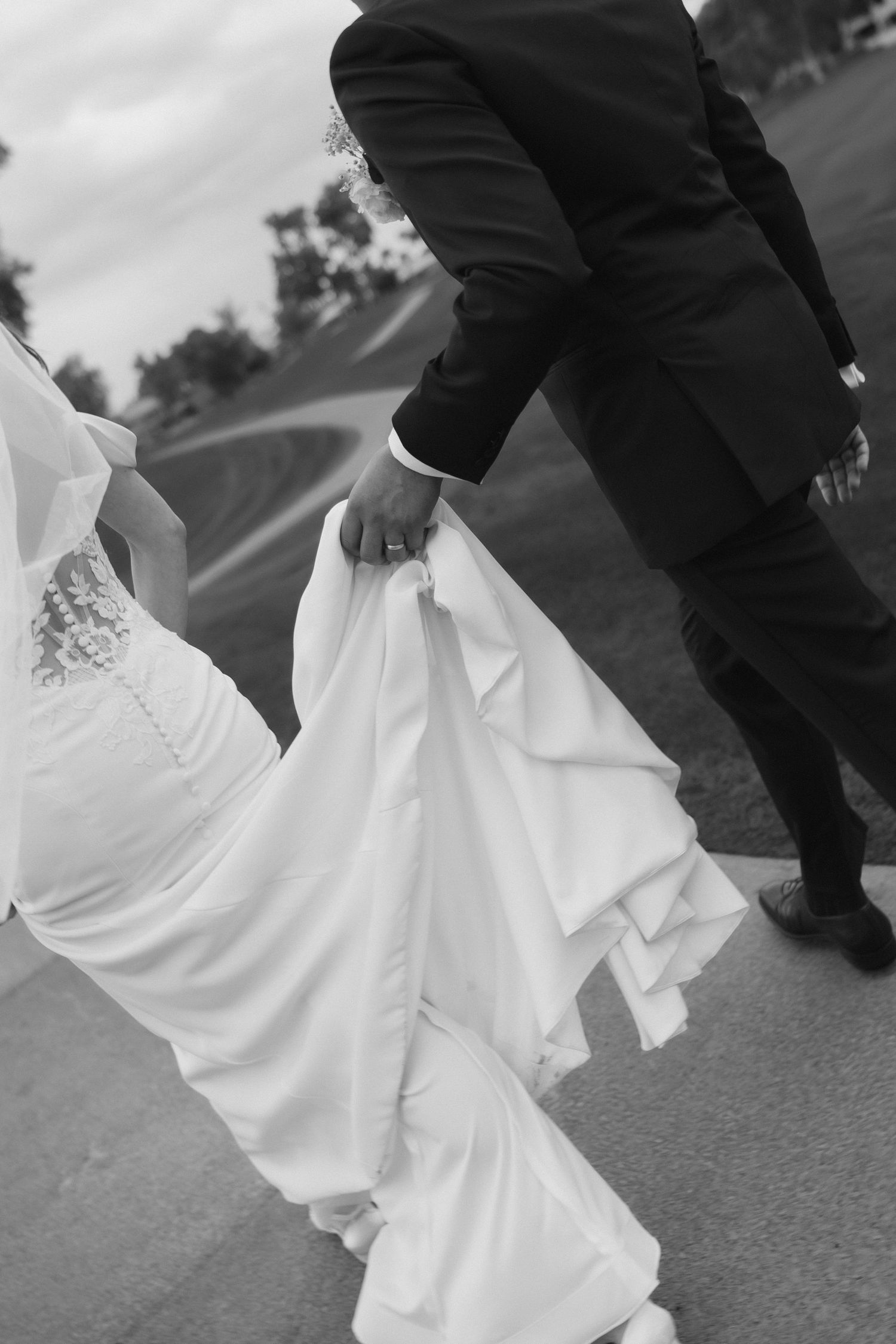 Black and white wedding photo series showing close-up details of bride's flowing white dress and groom's dark suit.
