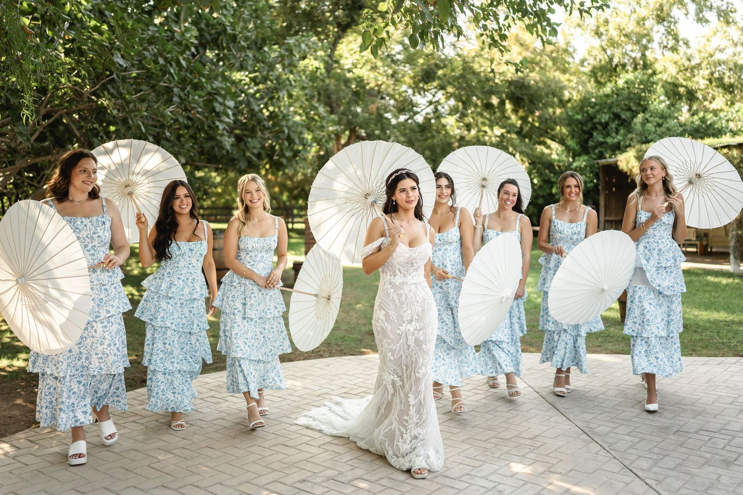 Bridesmaids in light blue dresses pose in a garden setting creating a graceful line formation.