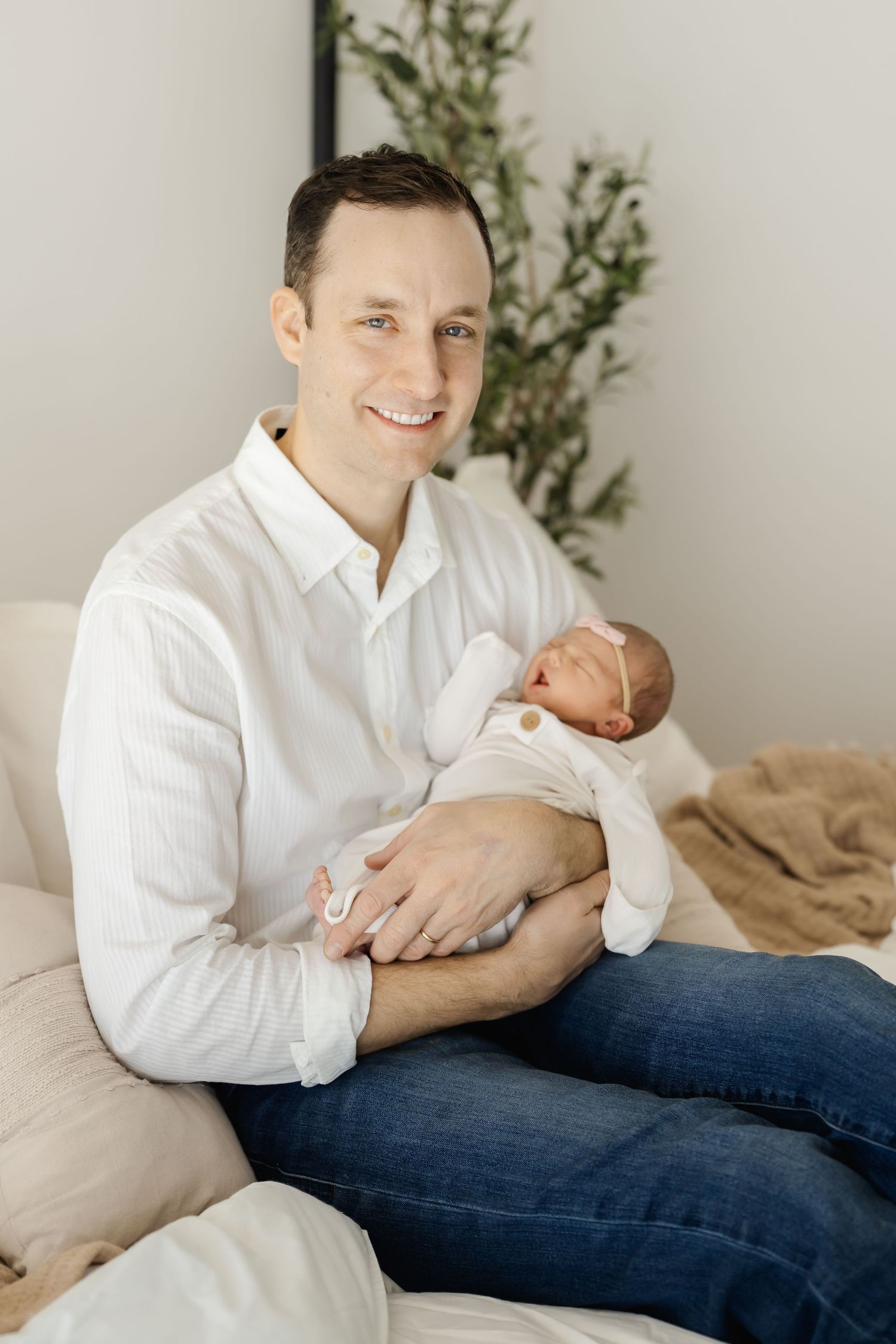 Parent holds newborn baby while sitting casually in white shirt and jeans.