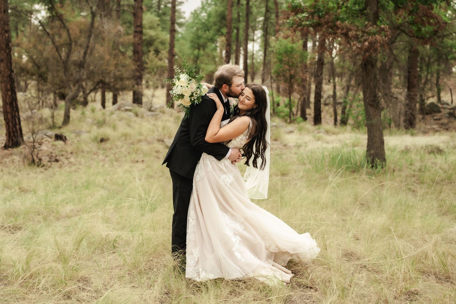 Two people share an intimate dance dip pose in a rustic outdoor forest setting with golden light.