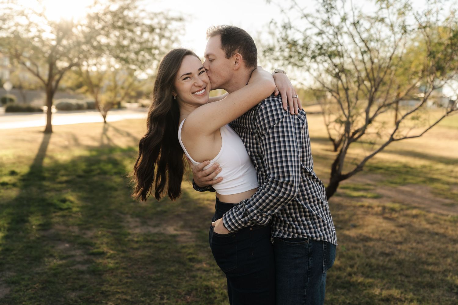 A couple embraces in a romantic sunset photoshoot at a scenic outdoor location with golden light filtering through trees.