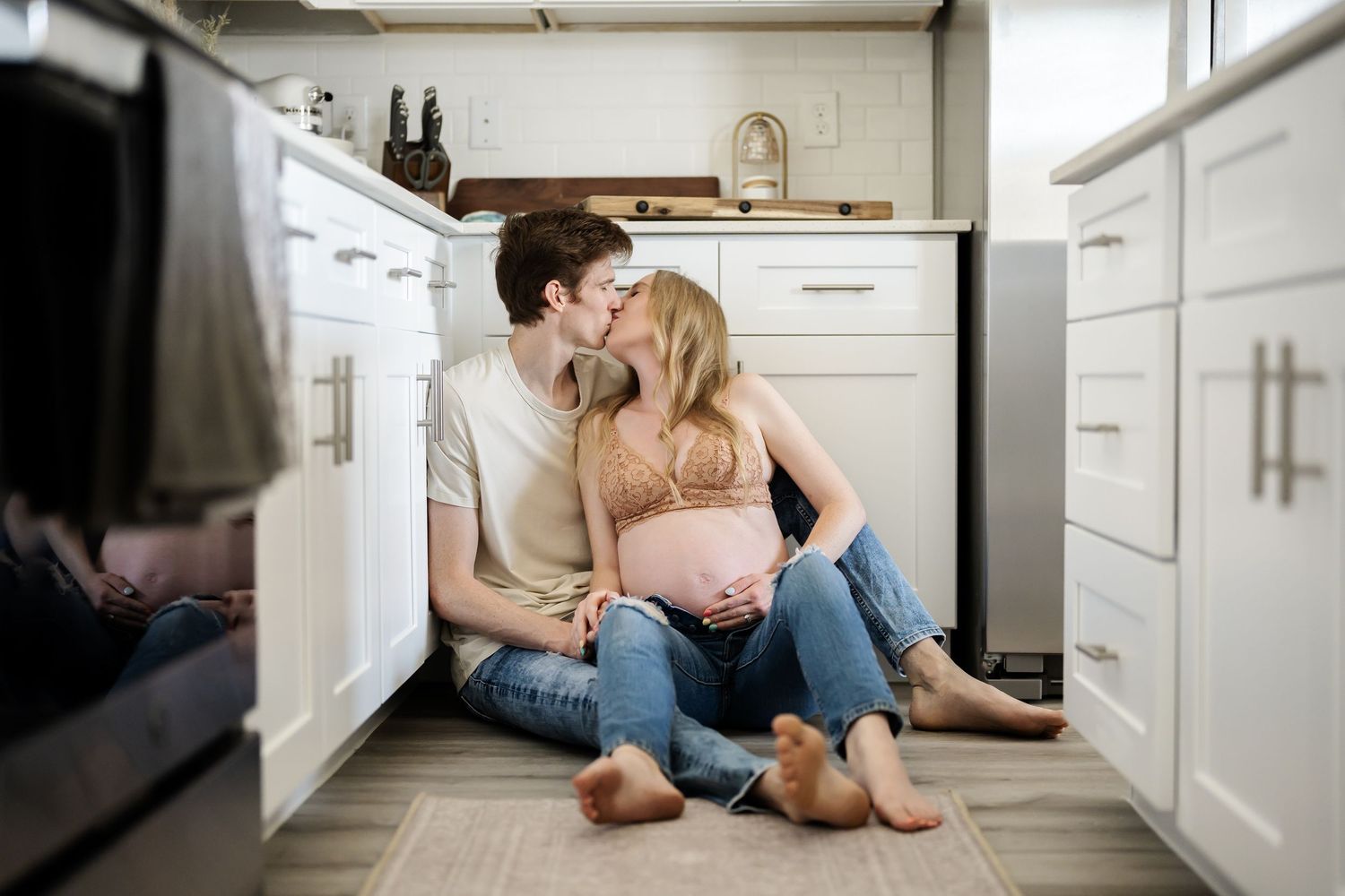 Person lying on kitchen floor between white cabinets with bare feet showing.