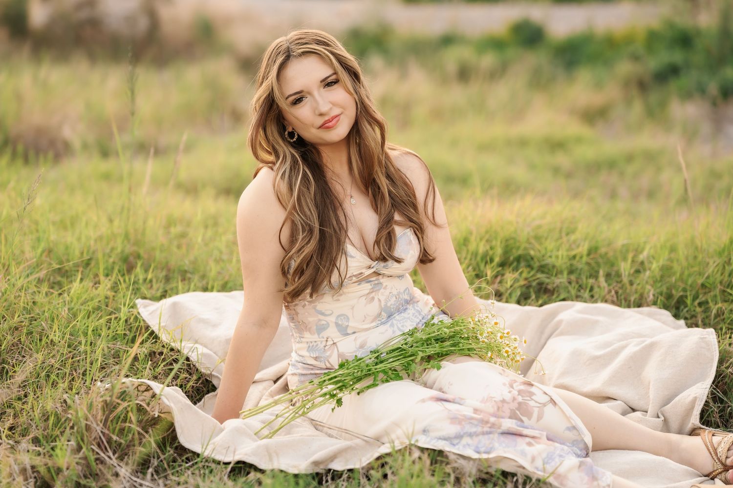 Model in white lace top reclining on grass during outdoor photo session.