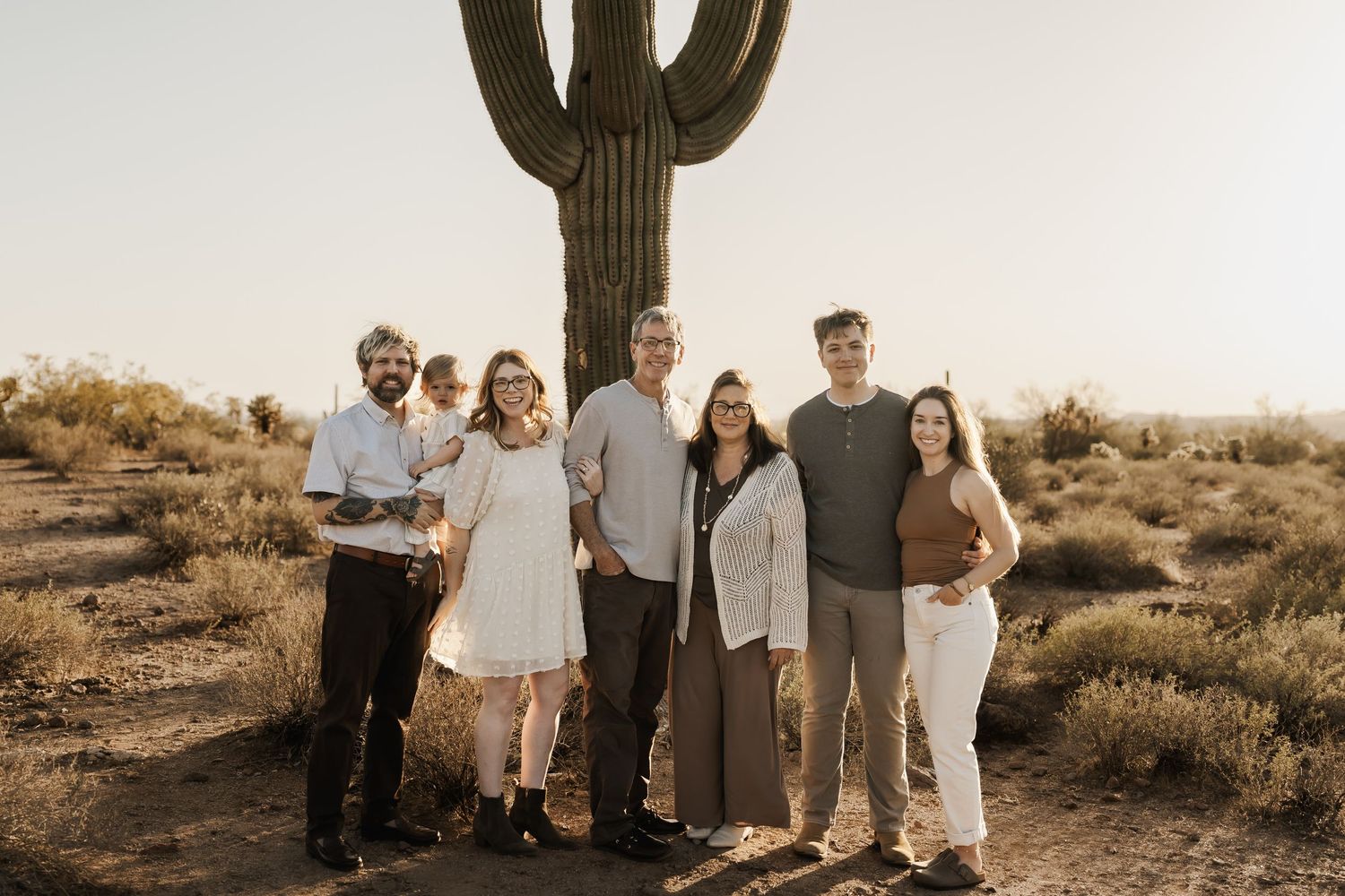 Desert landscape family photo with saguaro cactus and rocky formations at sunset.